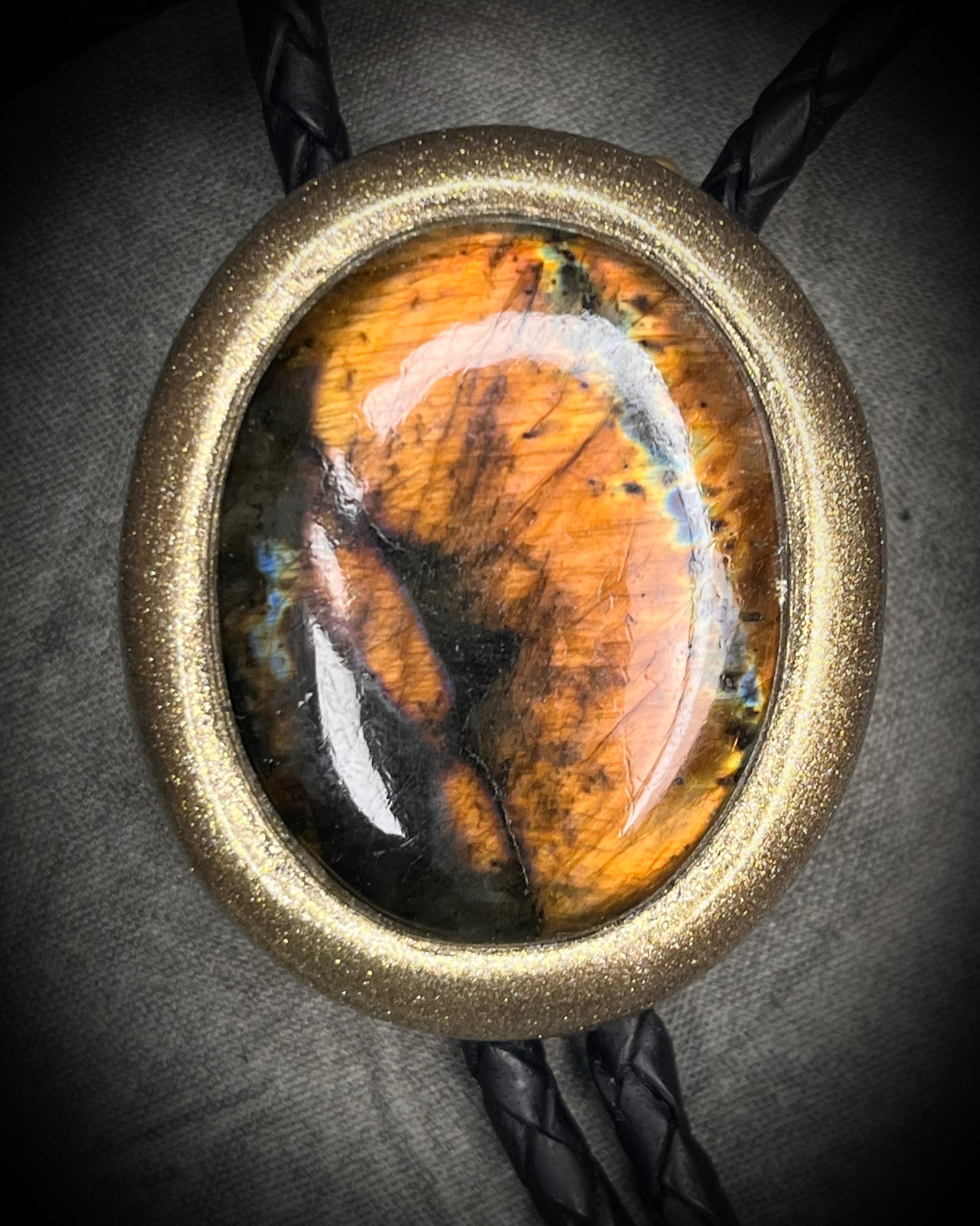 Glowing mystical orange labradorite bolo tie with blue stripe in a gold setting, black leather cord, and antique gold bolo tips. Handmade by Become Spellbound.