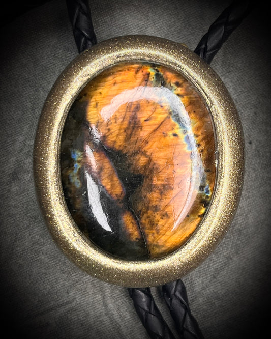Glowing mystical orange labradorite bolo tie with blue stripe in a gold setting, black leather cord, and antique gold bolo tips. Handmade by Become Spellbound.