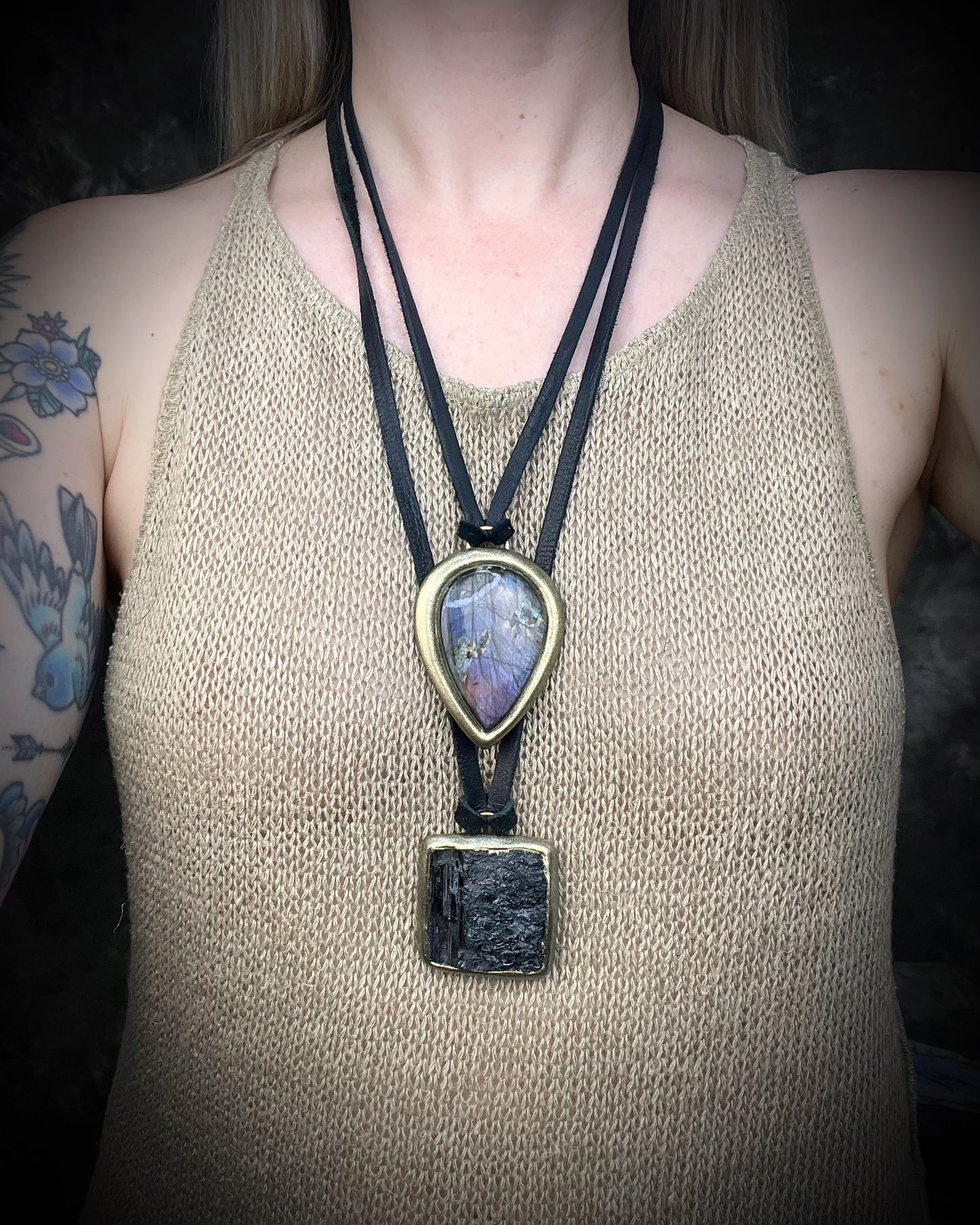 Gold finish, square shaped raw stone Black tourmaline grounding and protection pendant hung from black leather for an earthy adornment. layered here on a model with a purple labradorite necklace.