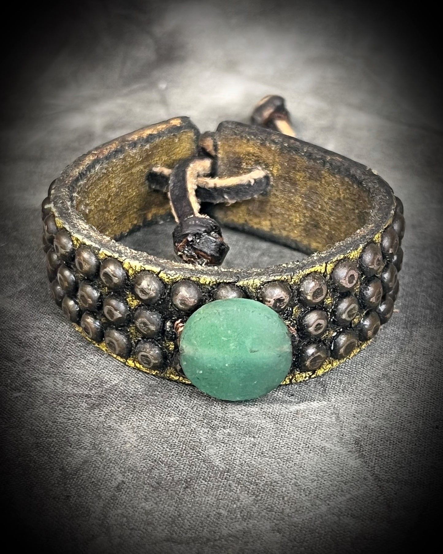 Golden brown studded leather cuff bracelet featuring a circular Green Aventurine focal stone. Rugged leatherwork with a lucky, calming stone, gift for him or her.