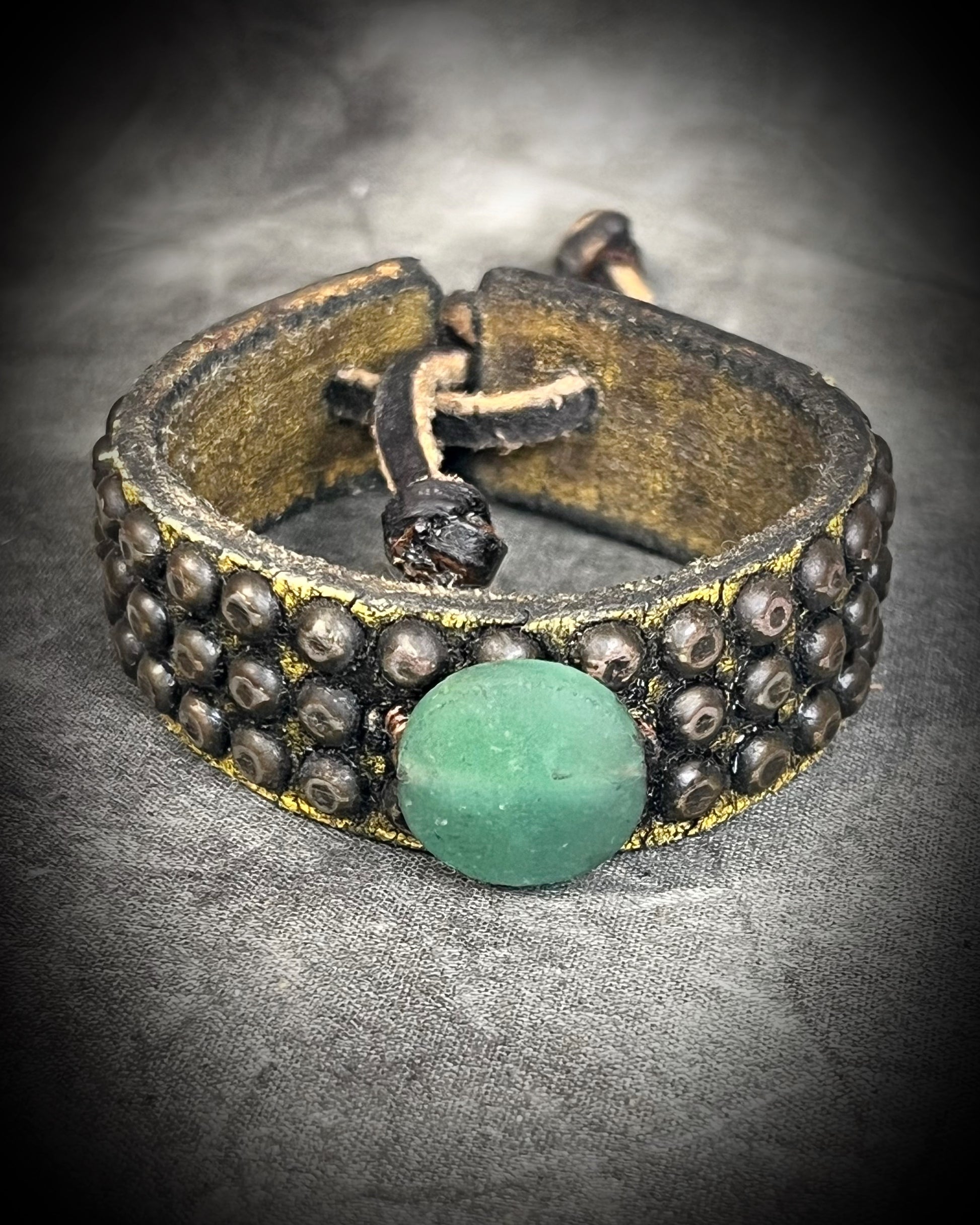 Golden brown studded leather cuff bracelet featuring a circular Green Aventurine focal stone. Rugged leatherwork with a lucky, calming stone, gift for him or her.