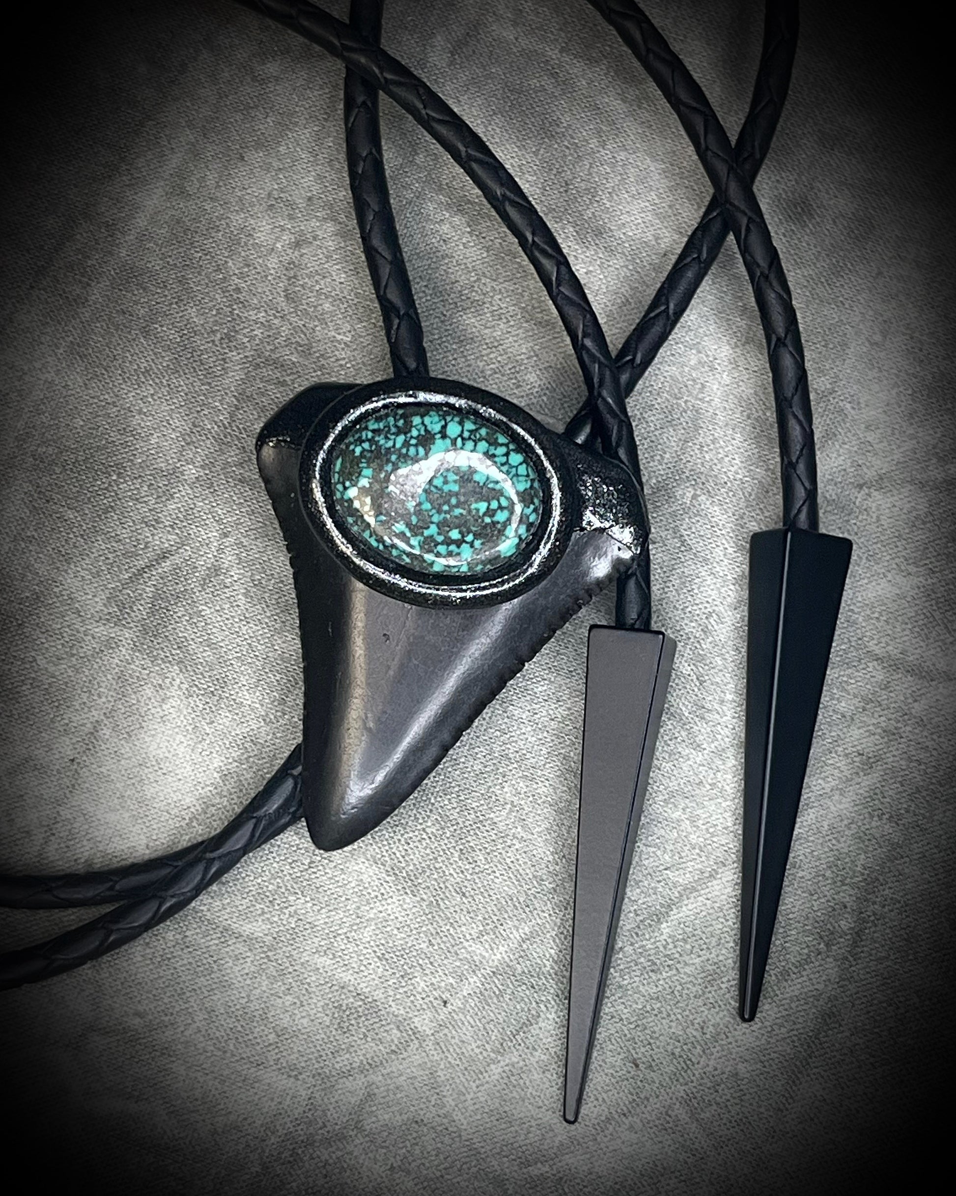 Great White shark tooth fossil bolo tie with black and turquoise-colored turquoise, black leather, black finish, and black spike tips.