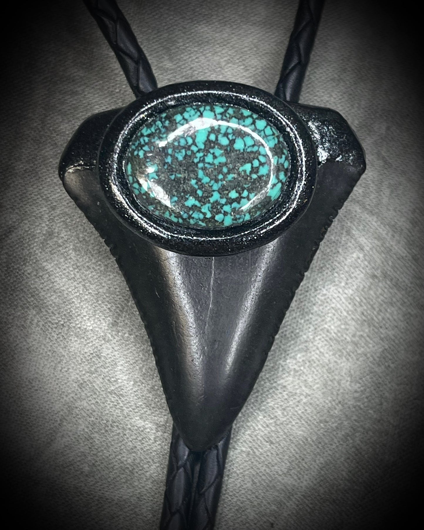 Great White shark tooth fossil bolo tie with black and turquoise-colored turquoise, black leather, black finish, and black spike tips.
