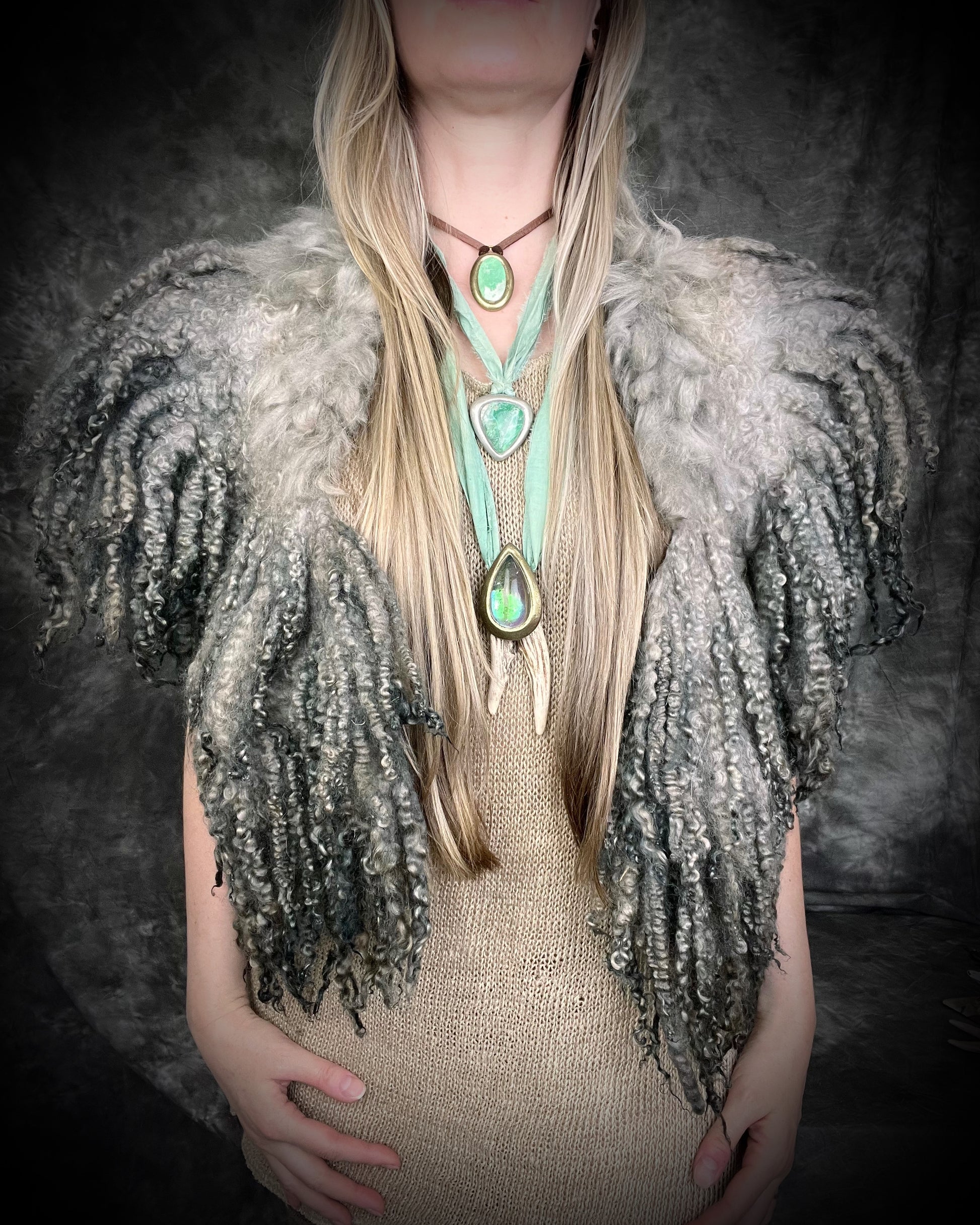 Person wearing a textured silver handmade merino wool shawl garment and multiple necklaces with heart-shaped pendants.