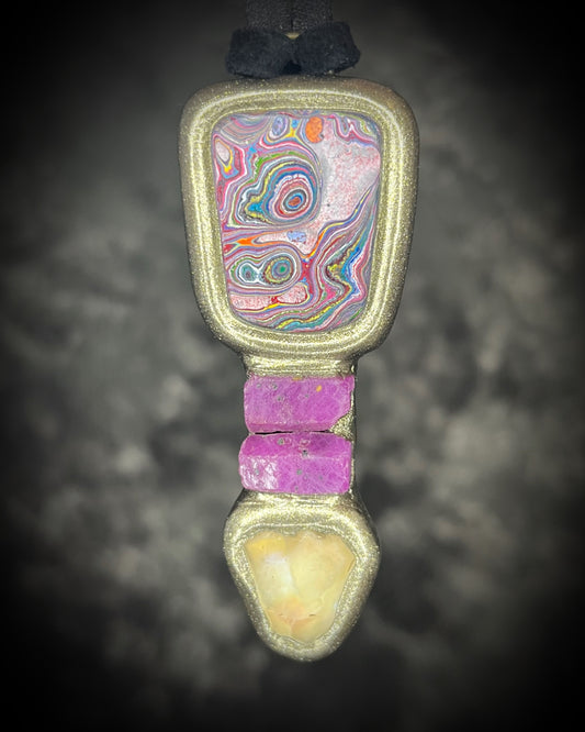 Hand-cut Cadillac Ranch Fordite cabochon with a ruby stack and Libyan Desert Glass in a sculptural gold-finish talisman on black leather, handmade by Become Spellbound in Baltimore, Maryland.