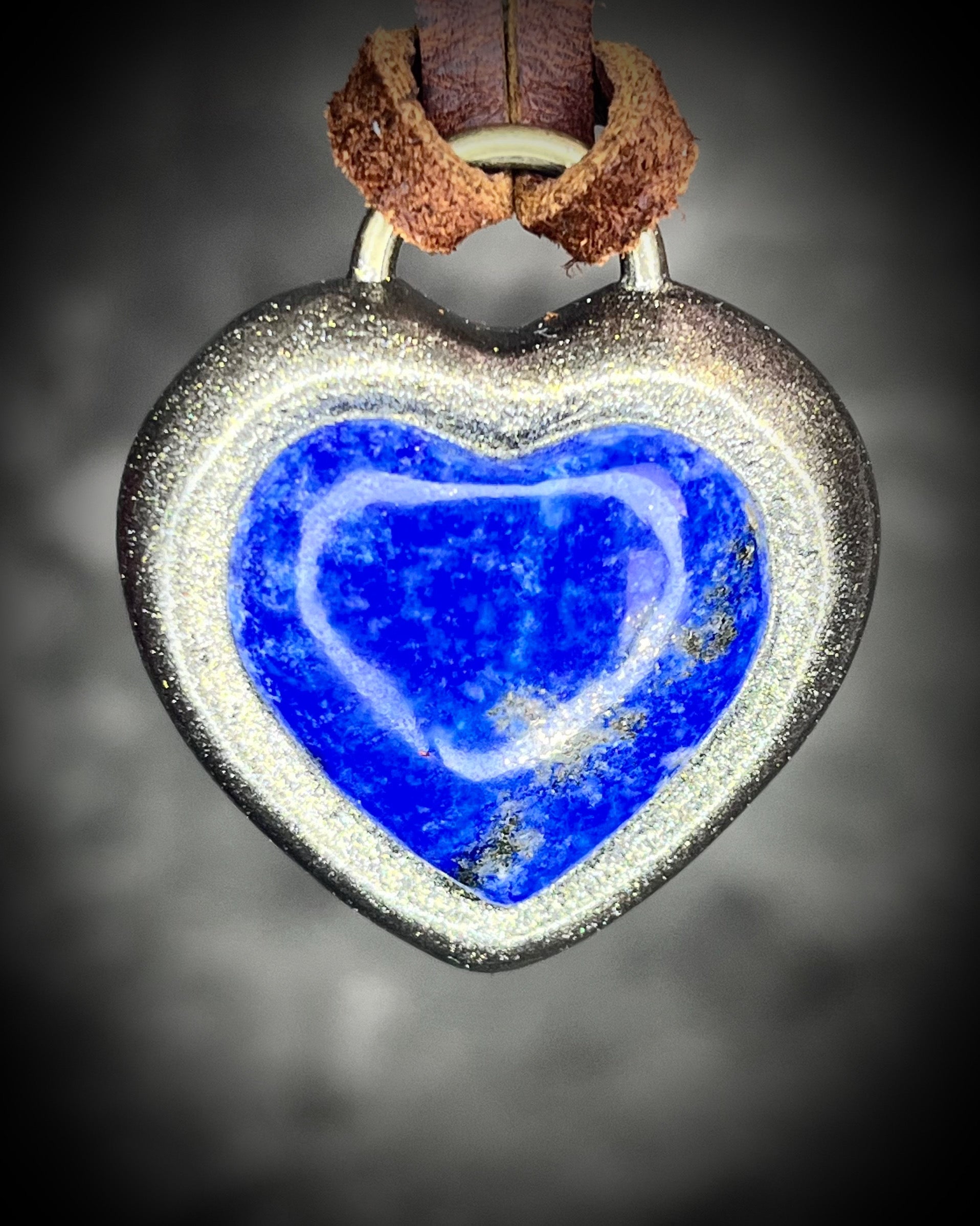 Handcrafted lapis lazuli heart pendant with gold finish on brown leather cord, glowing deep blue with pyrite flecks.