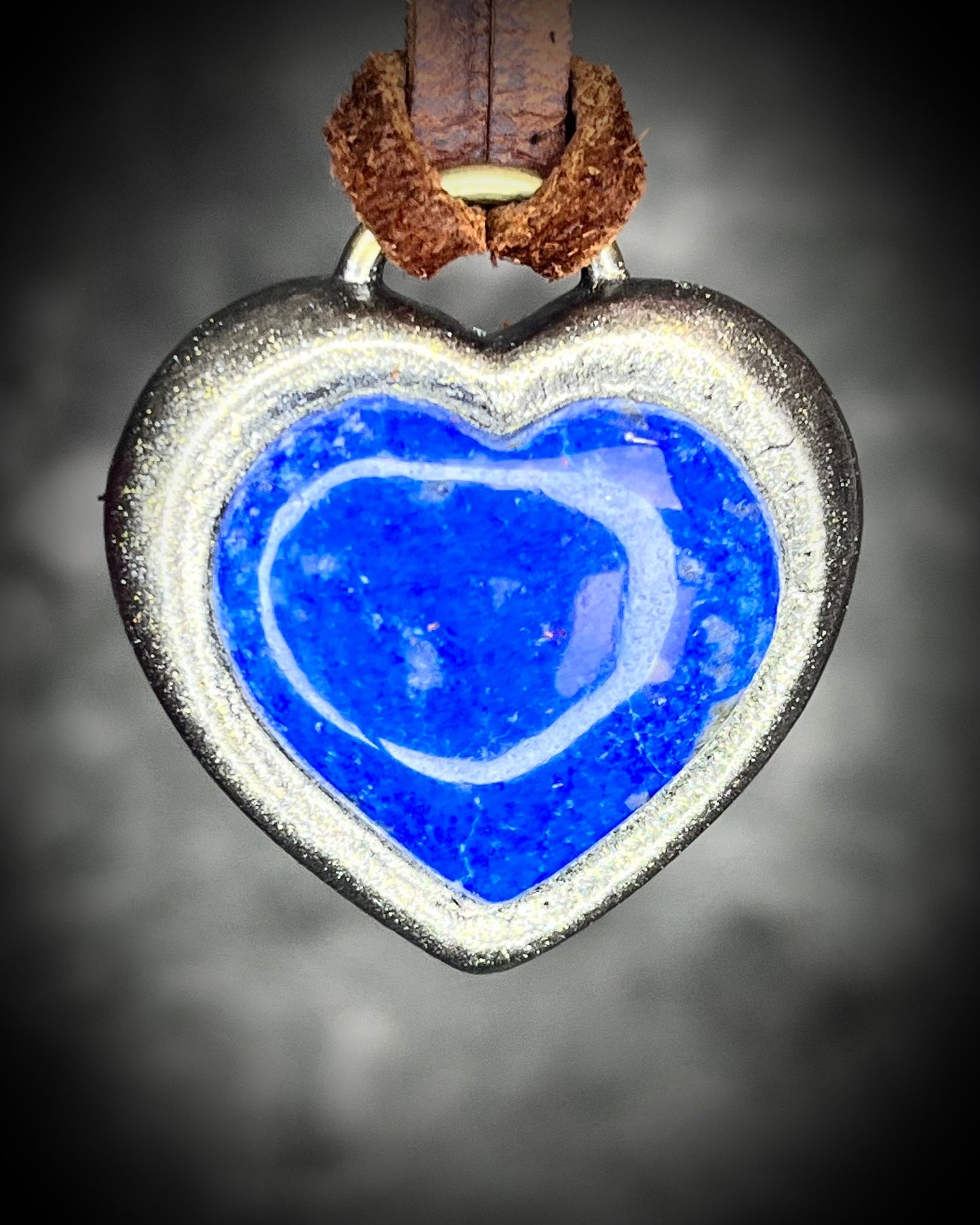 Handcrafted lapis lazuli heart pendant with gold finish on brown leather cord, glowing deep blue with pyrite flecks.