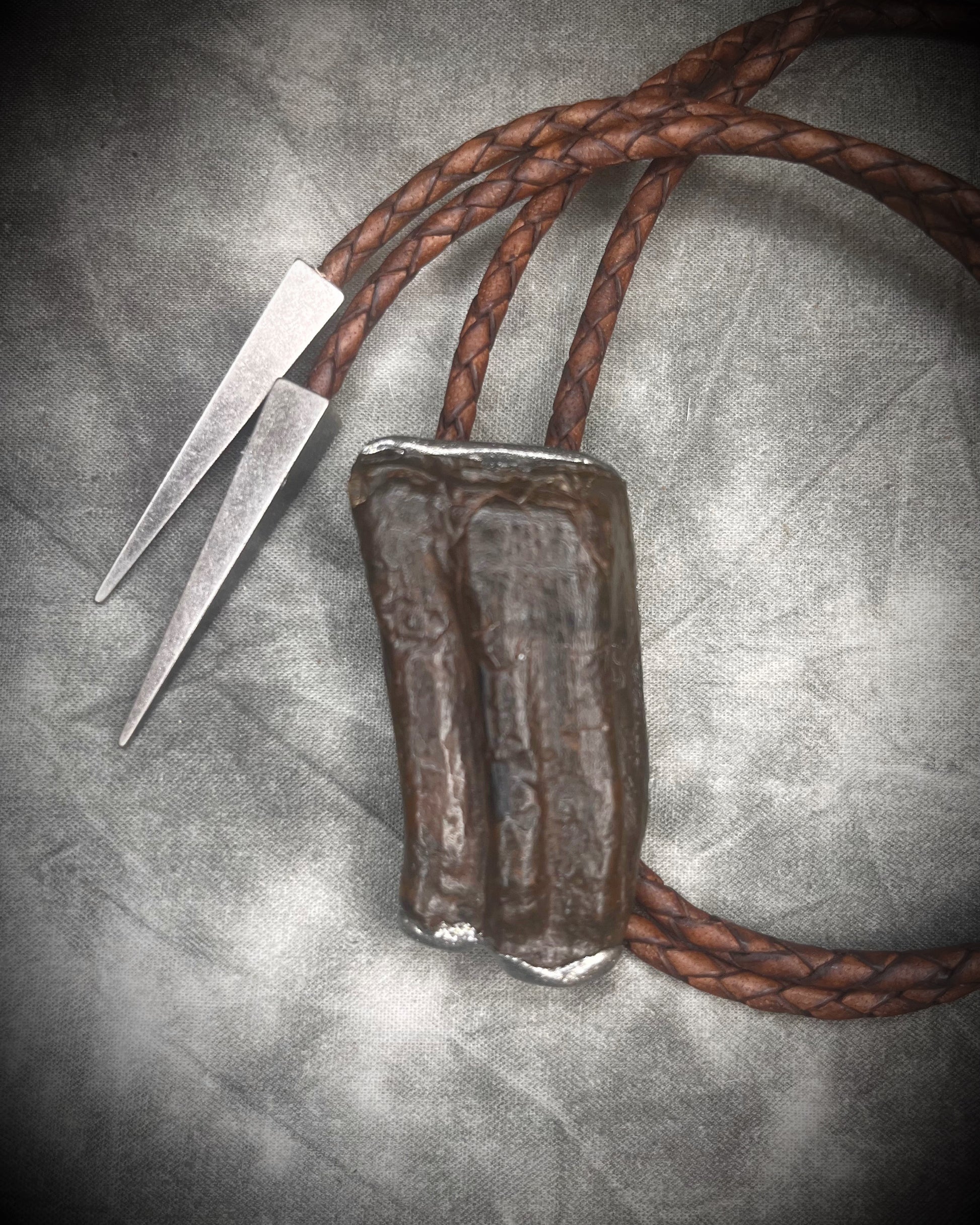 Handmade Equus bolo tie featuring horse tooth fossil centerpiece with gunmetal silver sculptural detailing, brass findings, spike tip ends, and leather cord bolo necklace. Natural history talisman for him, handmade in Baltimore Maryland.  