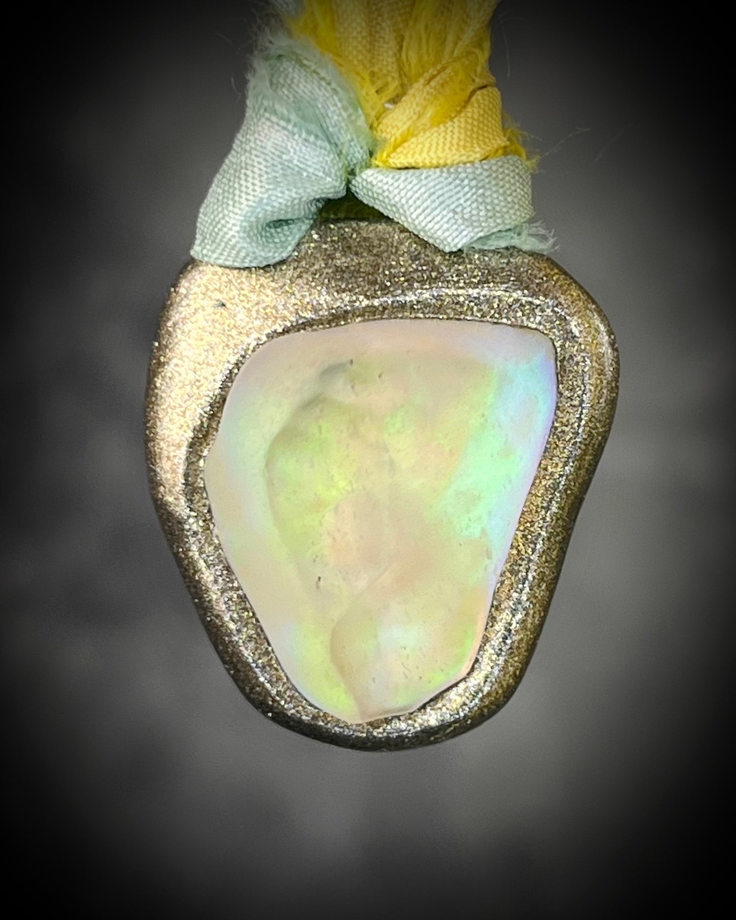Handmade Libyan Desert Glass talisman with luminous shifting flashes of green, gold, peach, and rose on sea green and yellow recycled silk by Become Spellbound.