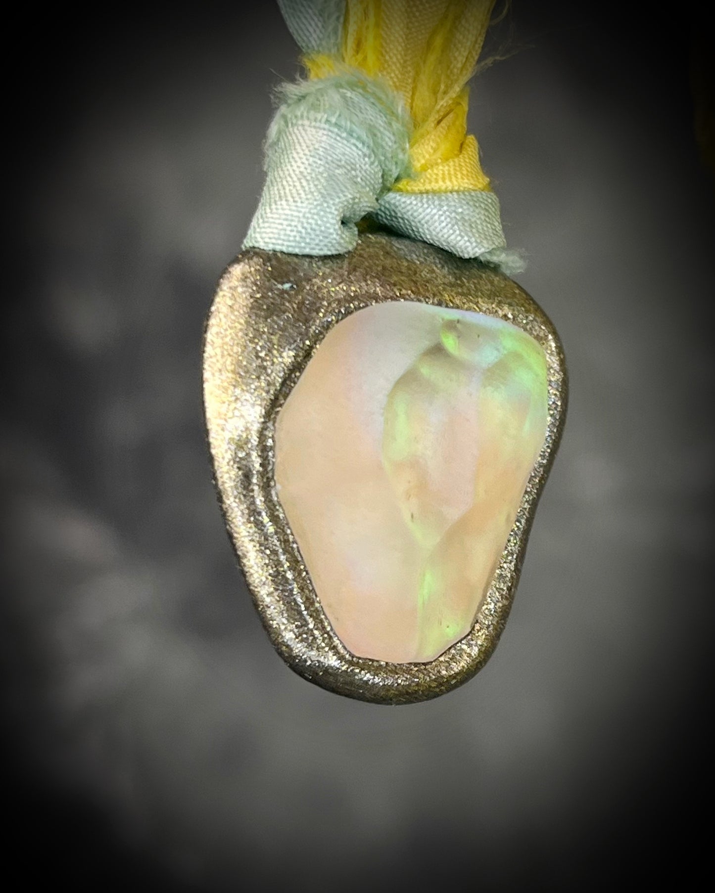 Handmade Libyan Desert Glass talisman with luminous shifting flashes of green, gold, peach, and rose on sea green and yellow recycled silk by Become Spellbound.