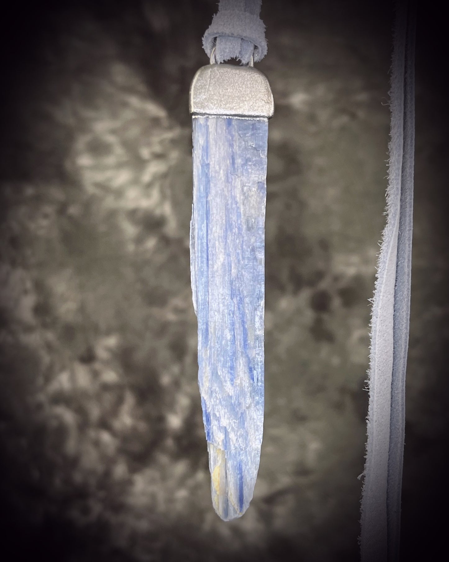 Handmade blue kyanite crystal necklace featuring a natural blue kyanite blade suspended from shimmering silver leather, artisan jewelry by Become Spellbound.