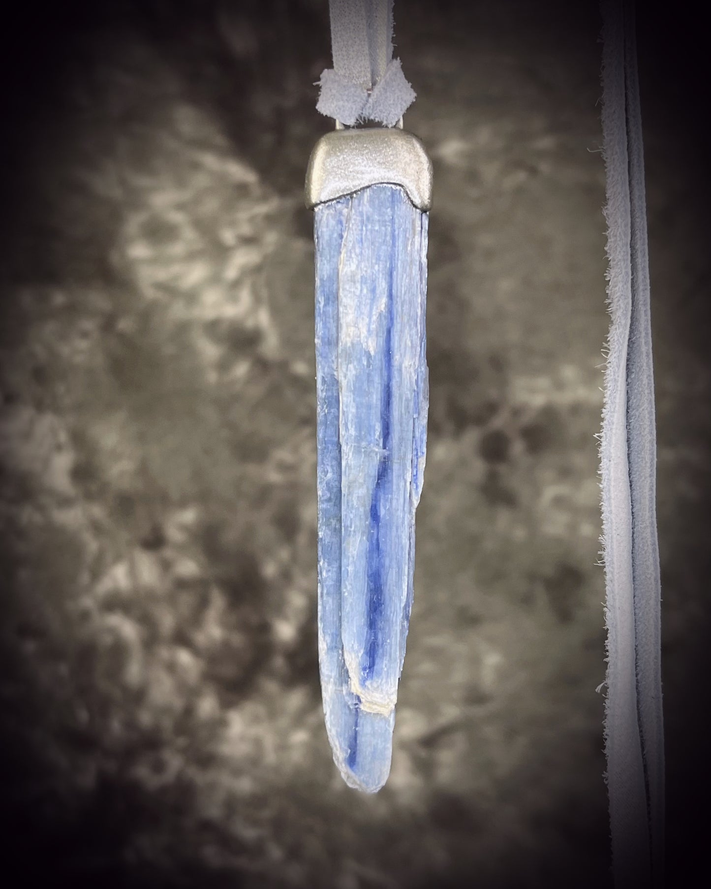 Handmade blue kyanite crystal necklace featuring a natural blue kyanite blade suspended from shimmering silver leather, artisan jewelry by Become Spellbound.