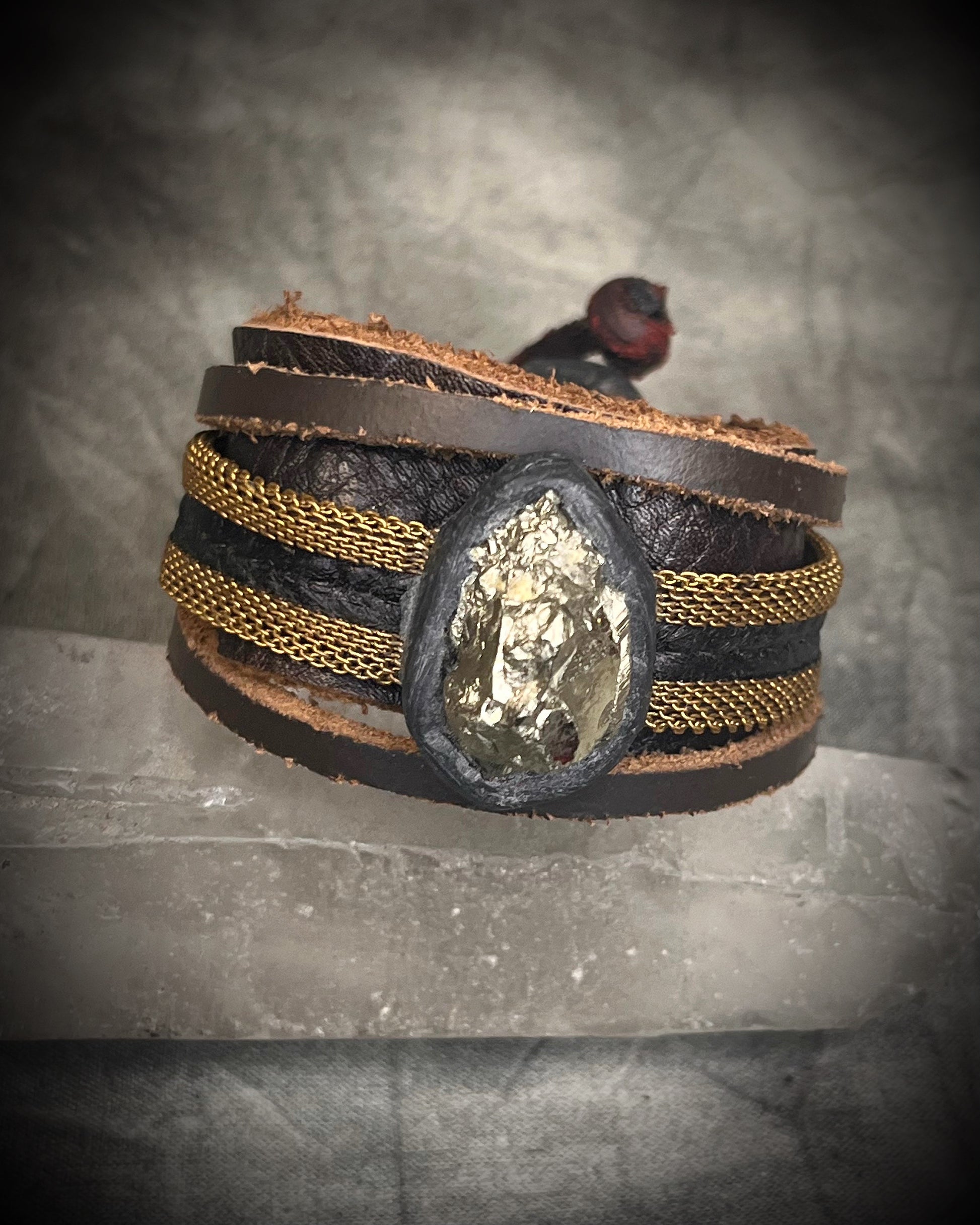 Handmade brown leather cuff bracelet with pyrite focal stone, woven brass chain, pyrite closure details, and adjustable leather tie closure by Anothai Hansen.