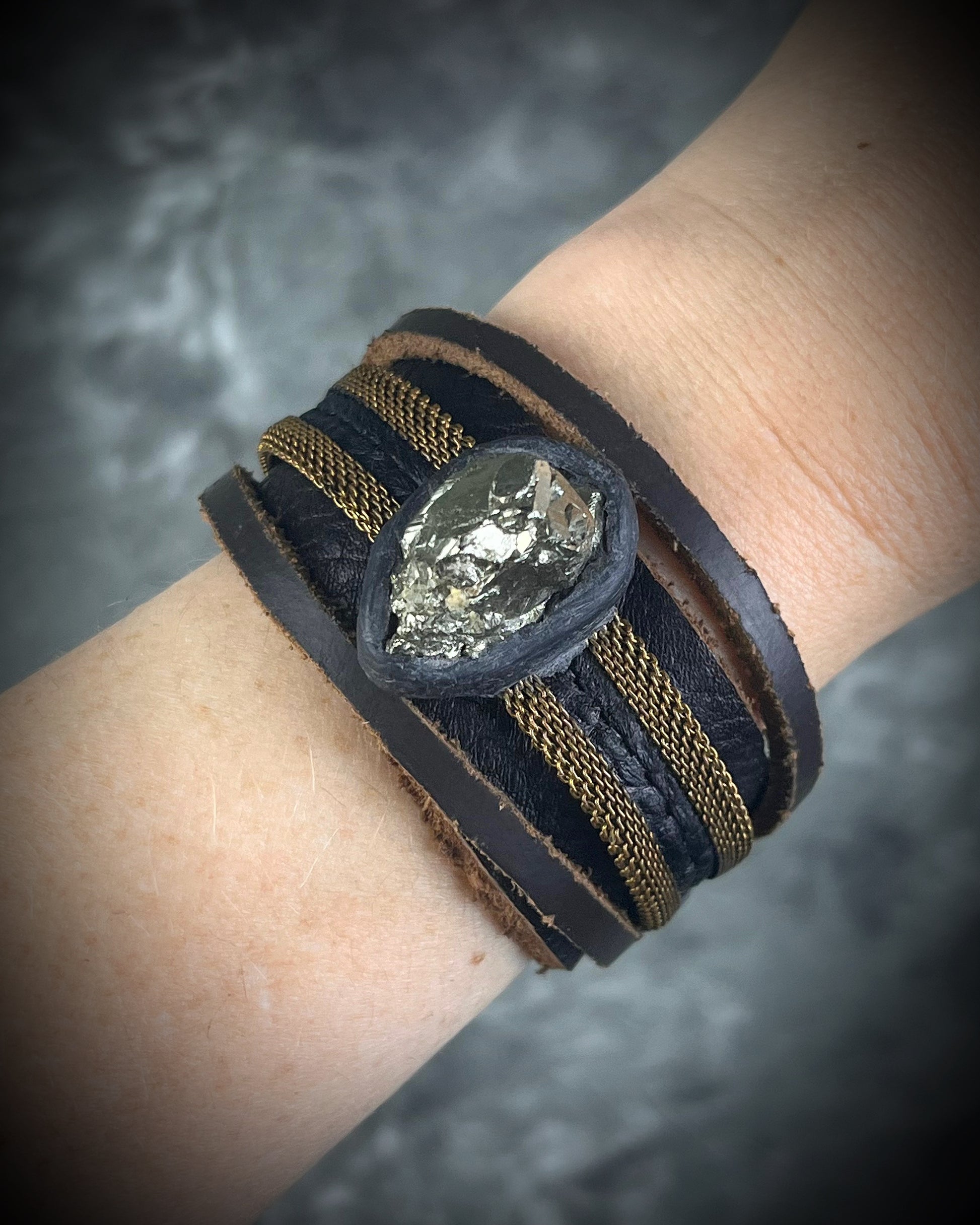Handmade brown leather cuff bracelet with pyrite focal stone, woven brass chain, pyrite closure details, and adjustable leather tie closure by Anothai Hansen.