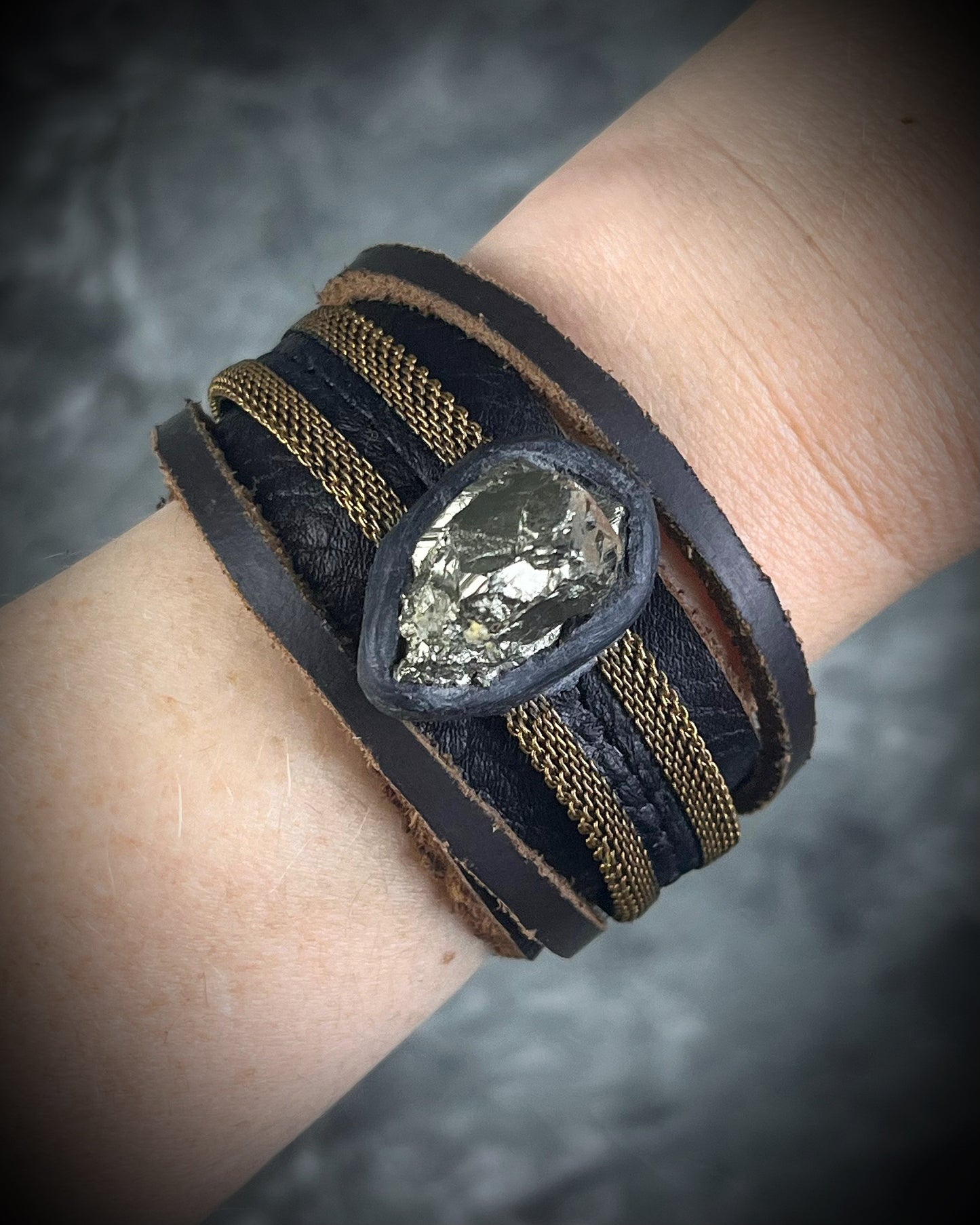 Handmade brown leather cuff bracelet with pyrite focal stone, woven brass chain, pyrite closure details, and adjustable leather tie closure by Anothai Hansen.