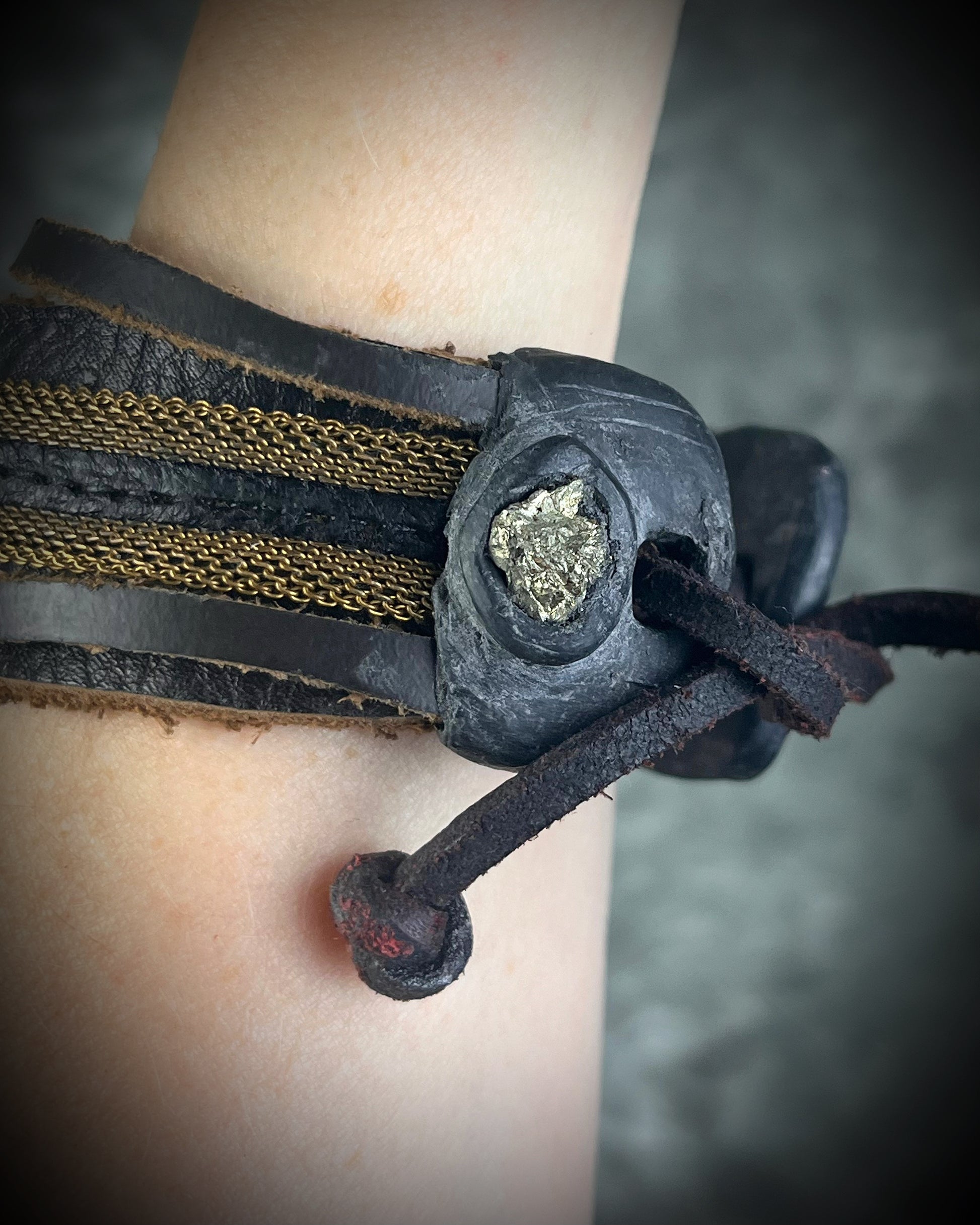 Handmade brown leather cuff bracelet with pyrite focal stone, woven brass chain, pyrite closure details, and adjustable leather tie closure by Anothai Hansen.