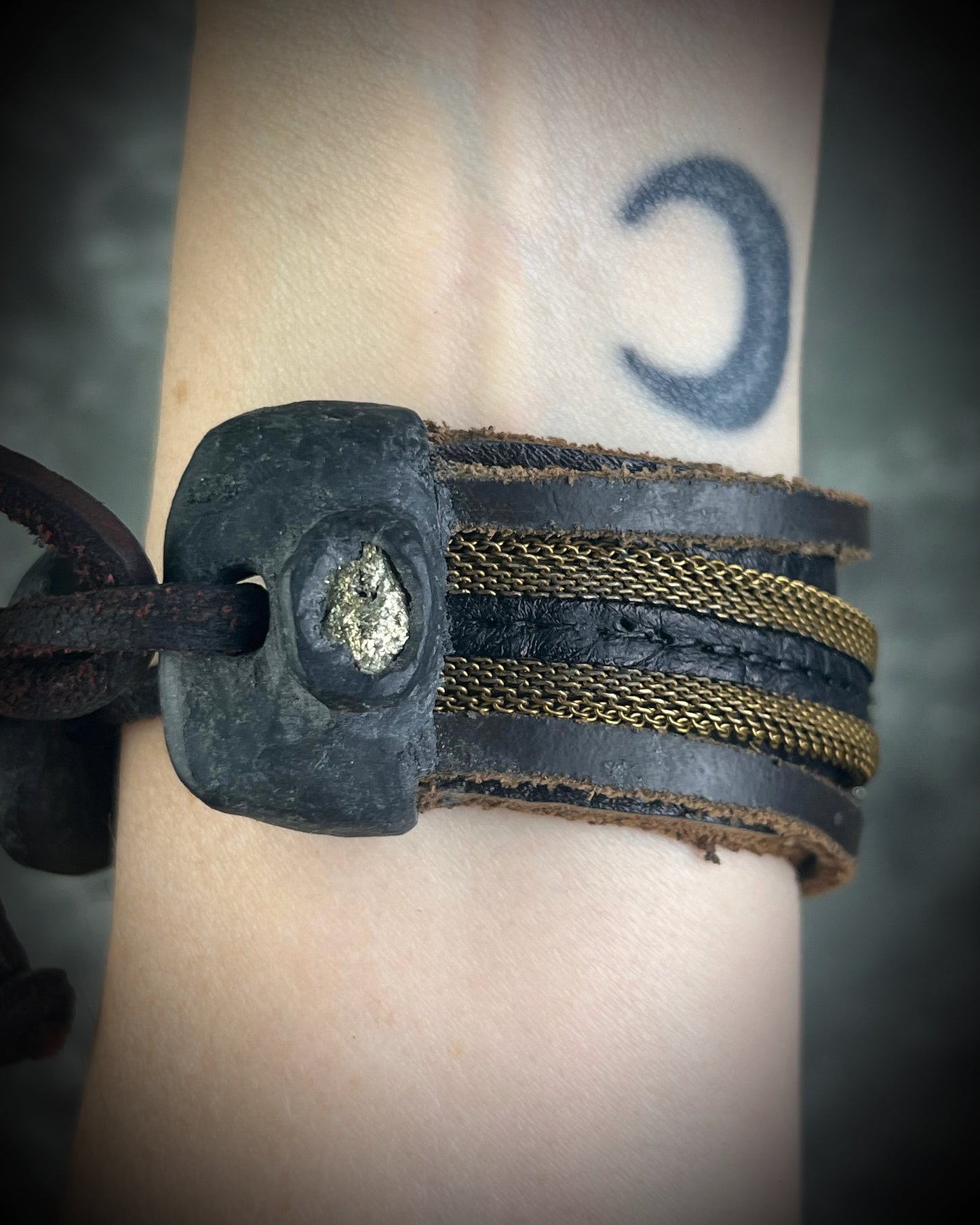 Handmade brown leather cuff bracelet with pyrite focal stone, woven brass chain, pyrite closure details, and adjustable leather tie closure by Anothai Hansen.