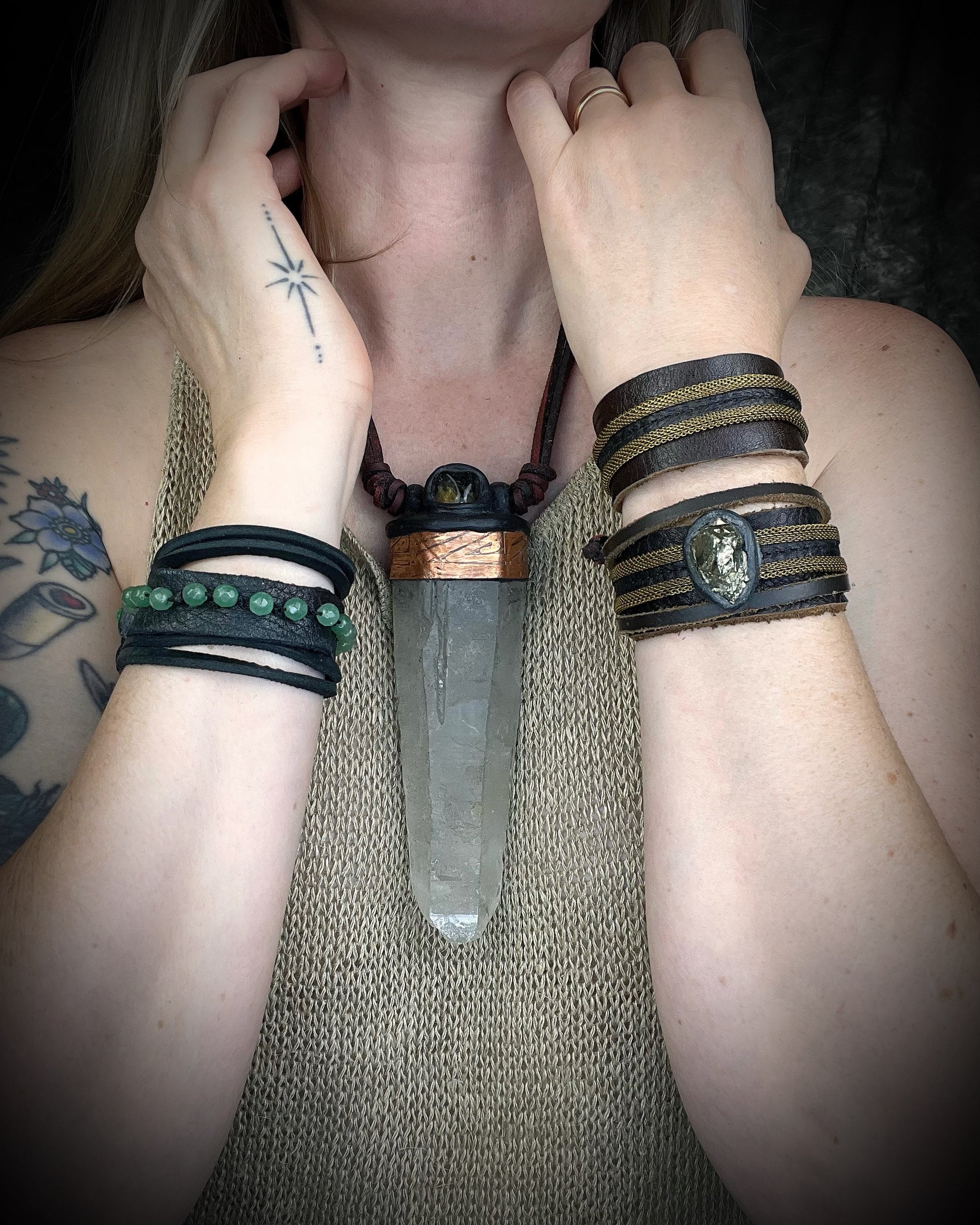 Handmade brown leather cuff bracelet with woven brass chain, rhodonite crystal details, and adjustable leather tie closure by Anothai Hansen.