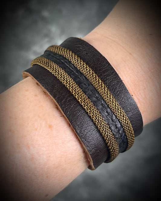 Handmade brown leather cuff bracelet with woven brass chain, rhodonite crystal details, and adjustable leather tie closure by Anothai Hansen.