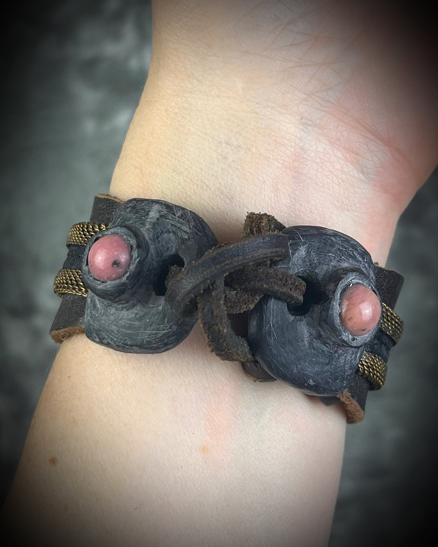 Handmade brown leather cuff bracelet with woven brass chain, rhodonite crystal details, and adjustable leather tie closure by Anothai Hansen.