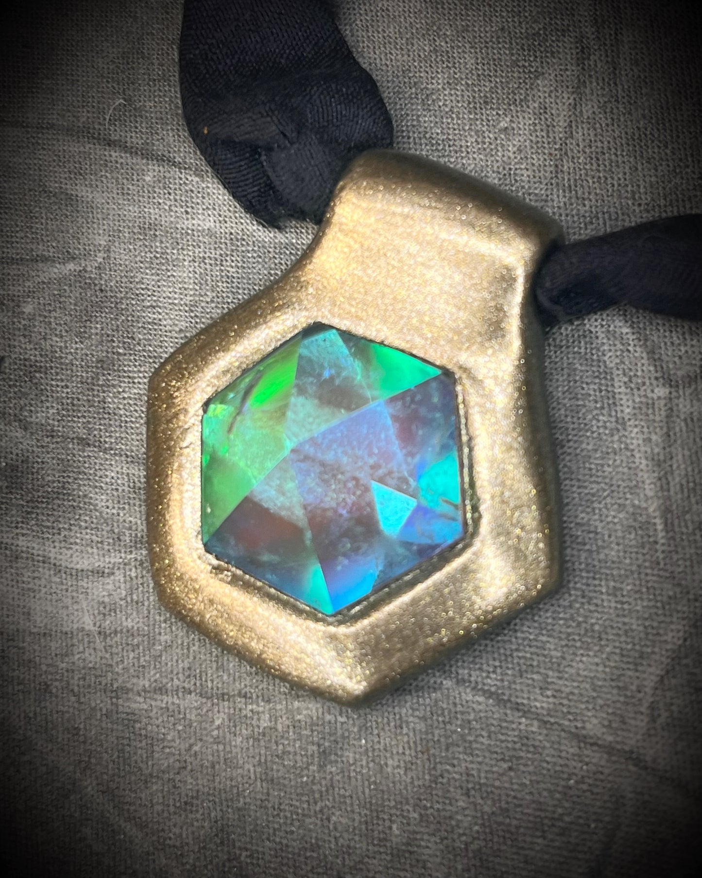 Handmade clear quartz crystal necklace with an aqua flash that feels oceanic and beachy. Framed in gold in a hexagon shape and hung from black recycled silk, this pendant feels like an unearthed treasure. Summer jewelry at its finest!