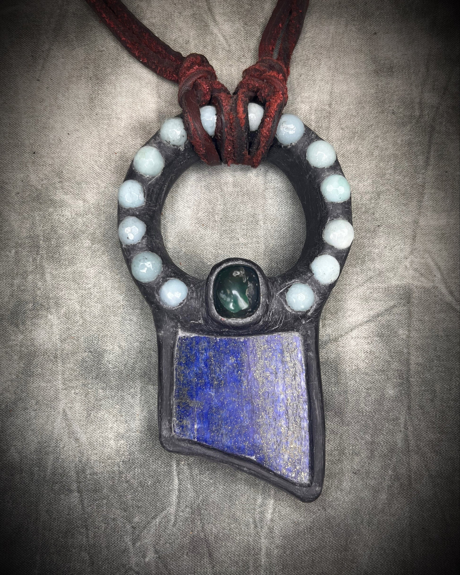 Handmade lapis lazuli slab necklace with aquamarine halo, bloodstone focal stone, deep red leather tie closure, and aquamarine tassel details by Anothai Hansen.