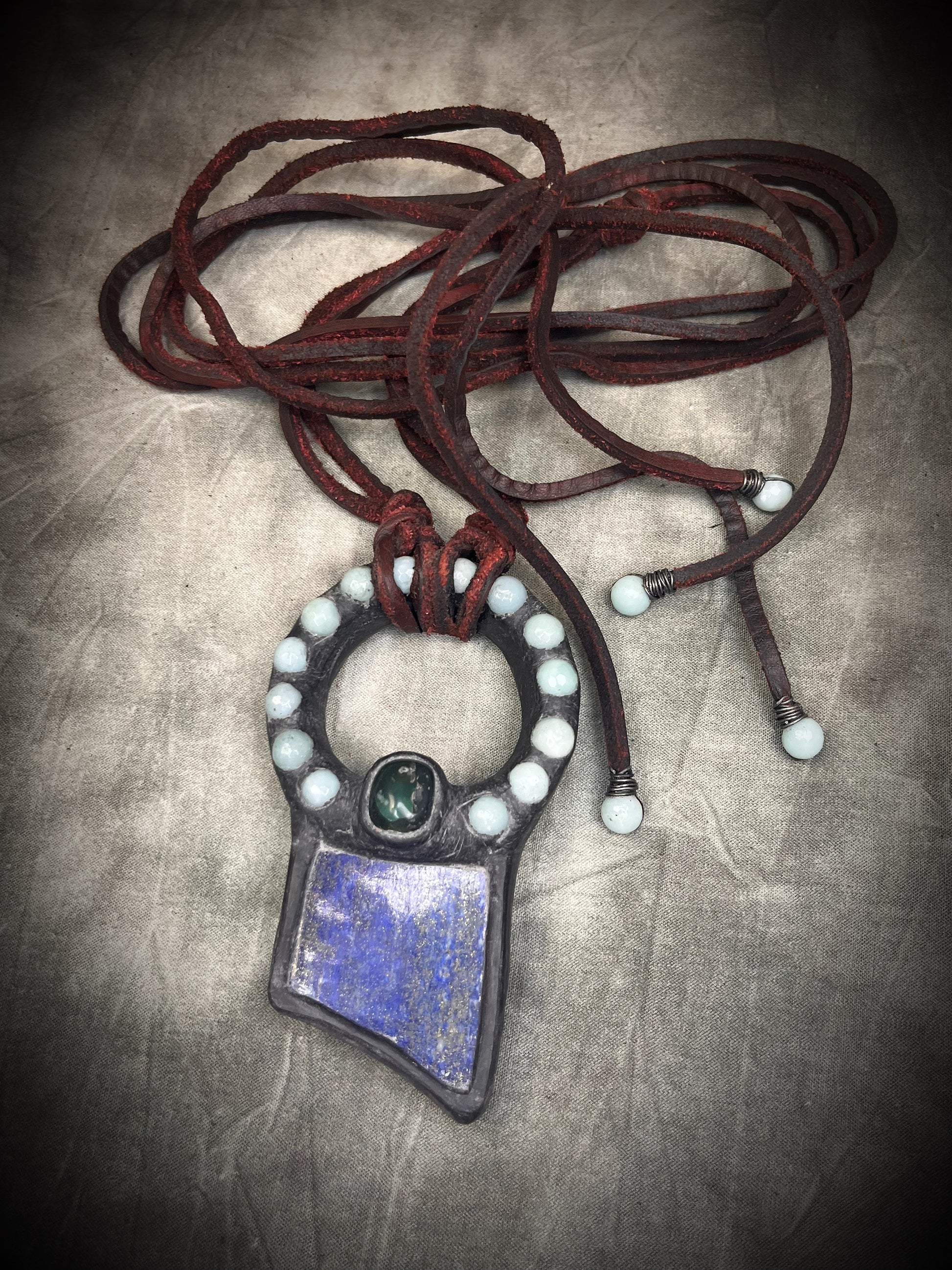 Handmade lapis lazuli slab necklace with aquamarine halo, bloodstone focal stone, deep red leather tie closure, and aquamarine tassel details by Anothai Hansen.