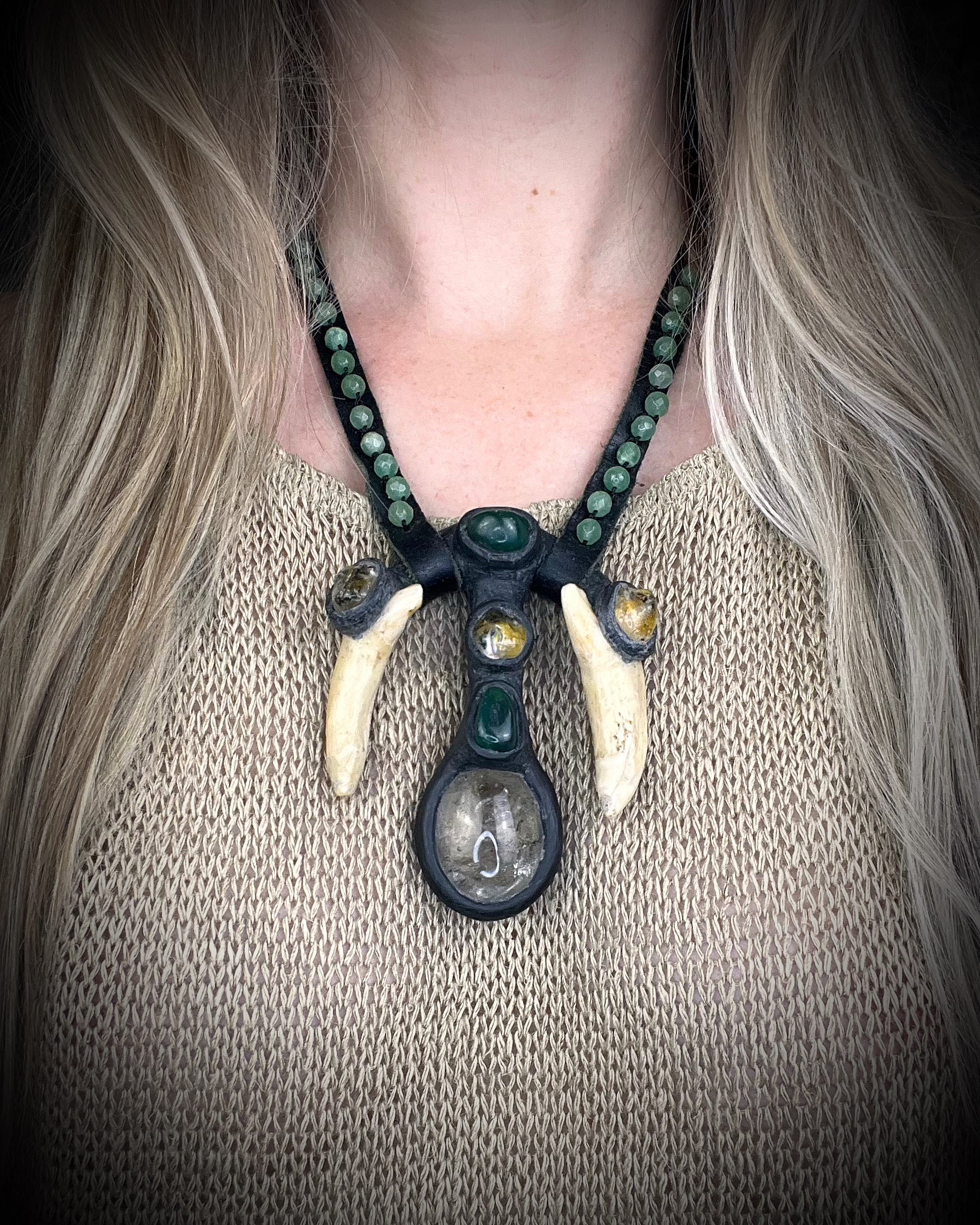 Handmade leather talisman with quartz, bloodstone, citrine, green aventurine, animal teeth, studded leather, and handmade wire clasp by Anothai Hansen.