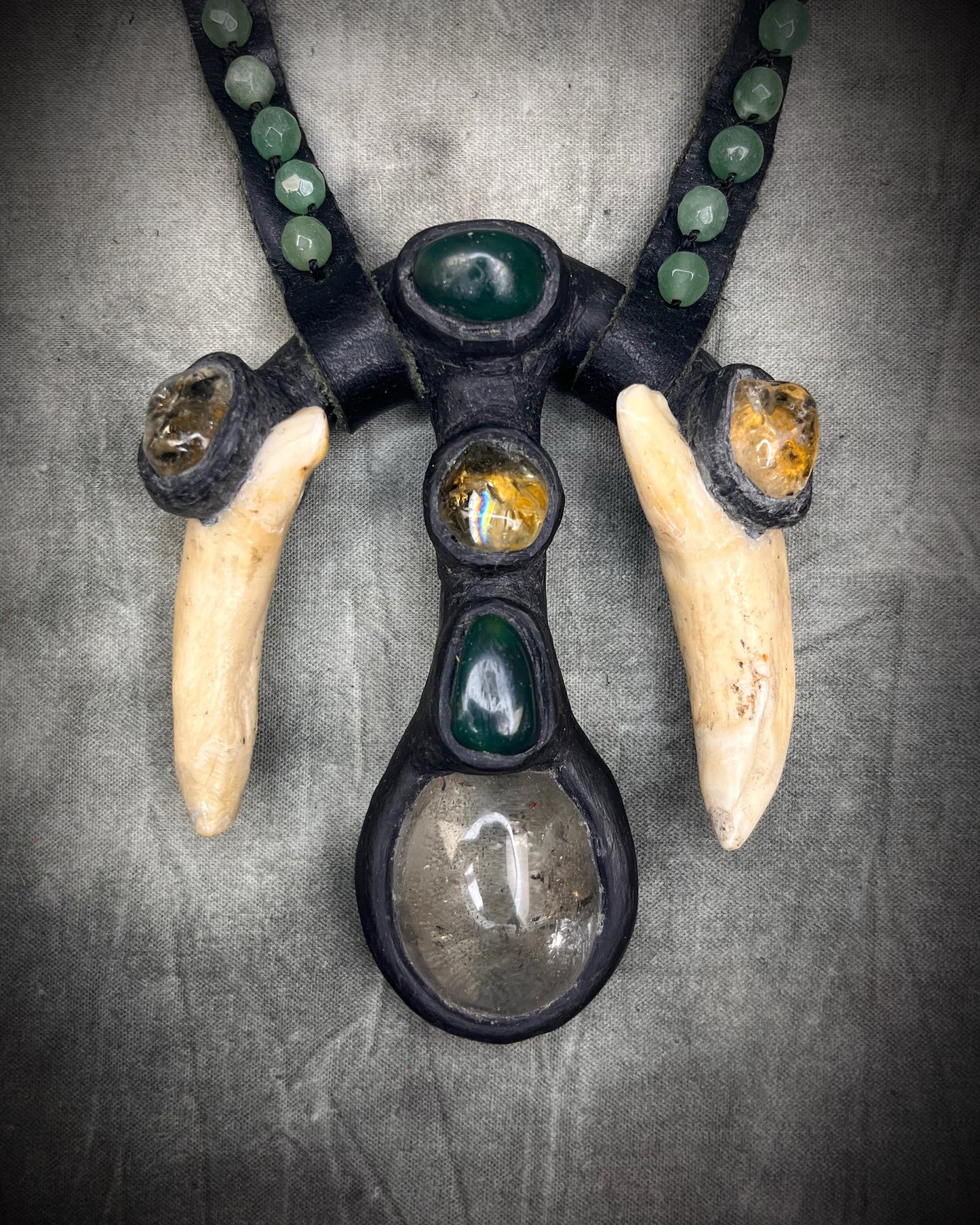 Handmade leather talisman with quartz, bloodstone, citrine, green aventurine, animal teeth, studded leather, and handmade wire clasp by Anothai Hansen.