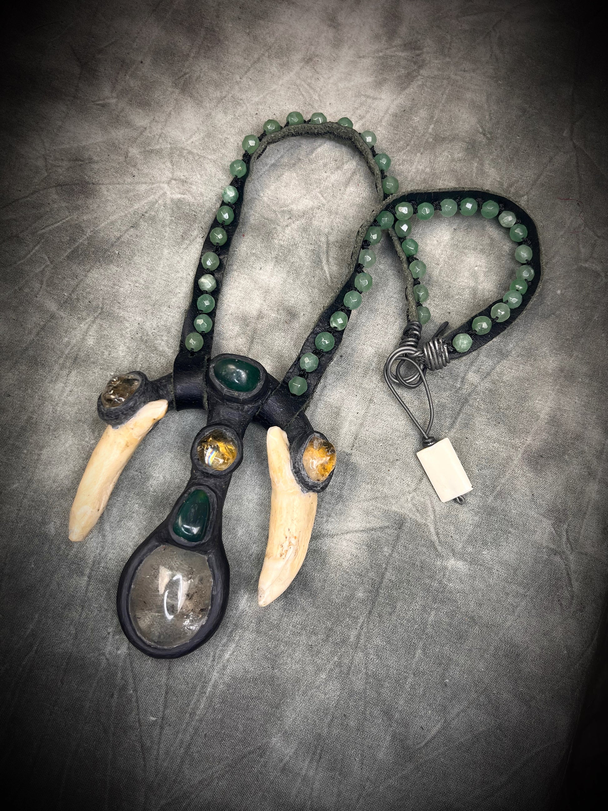Handmade leather talisman with quartz, bloodstone, citrine, green aventurine, animal teeth, studded leather, and handmade wire clasp by Anothai Hansen.