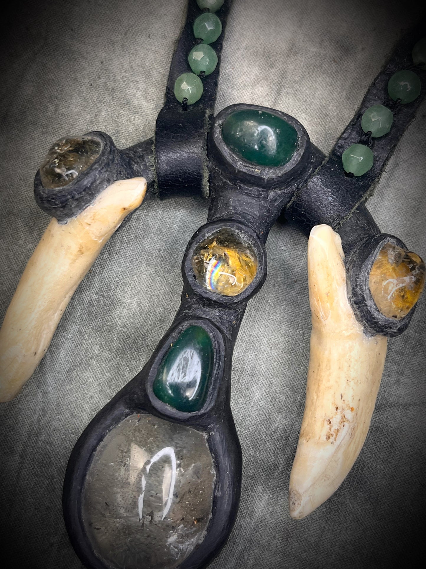 Handmade leather talisman with quartz, bloodstone, citrine, green aventurine, animal teeth, studded leather, and handmade wire clasp by Anothai Hansen.