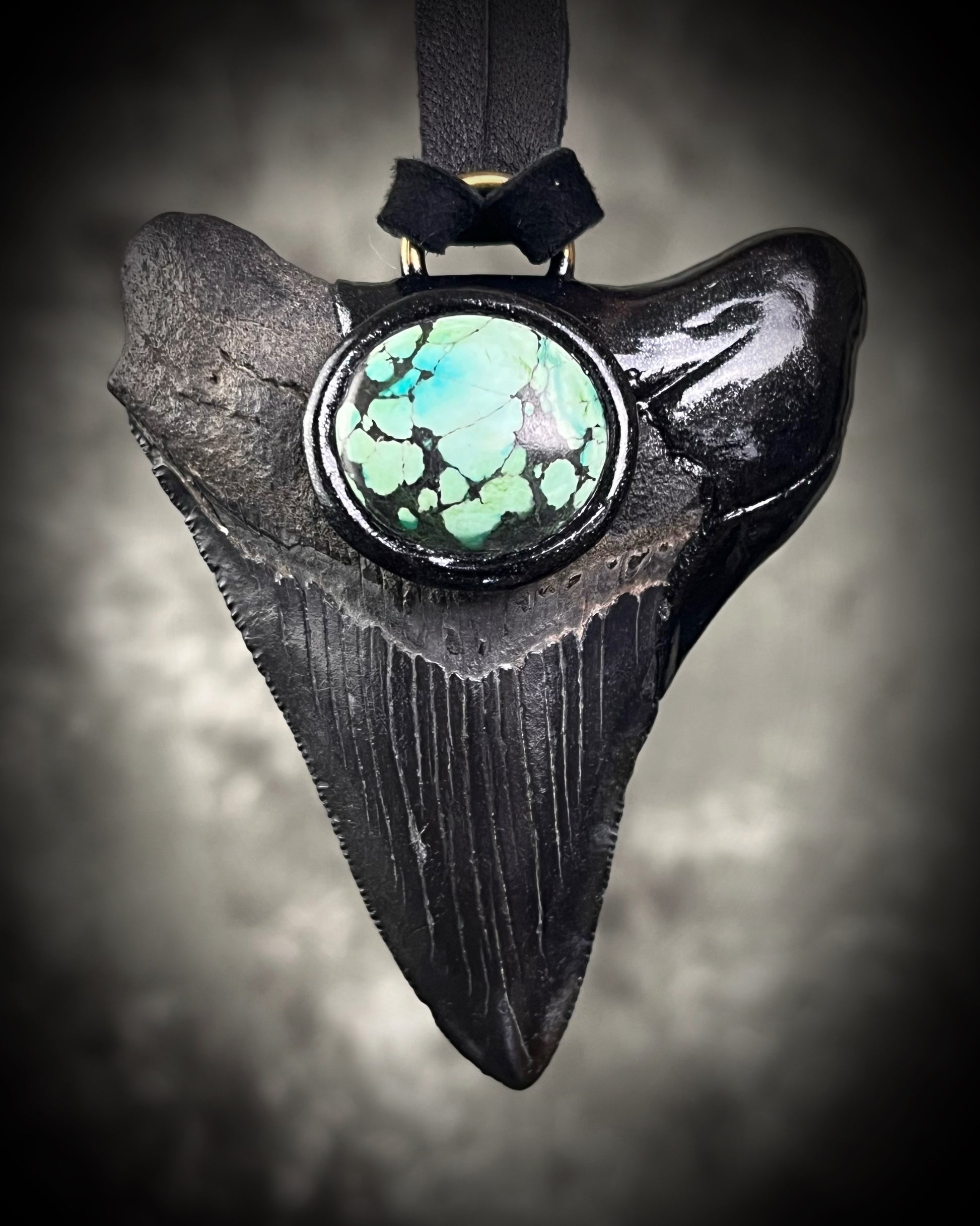Handmade megalodon tooth talisman with natural turquoise accents, black finish, and black leather cord, featuring a fossilized prehistoric shark tooth transformed into a bold statement necklace.