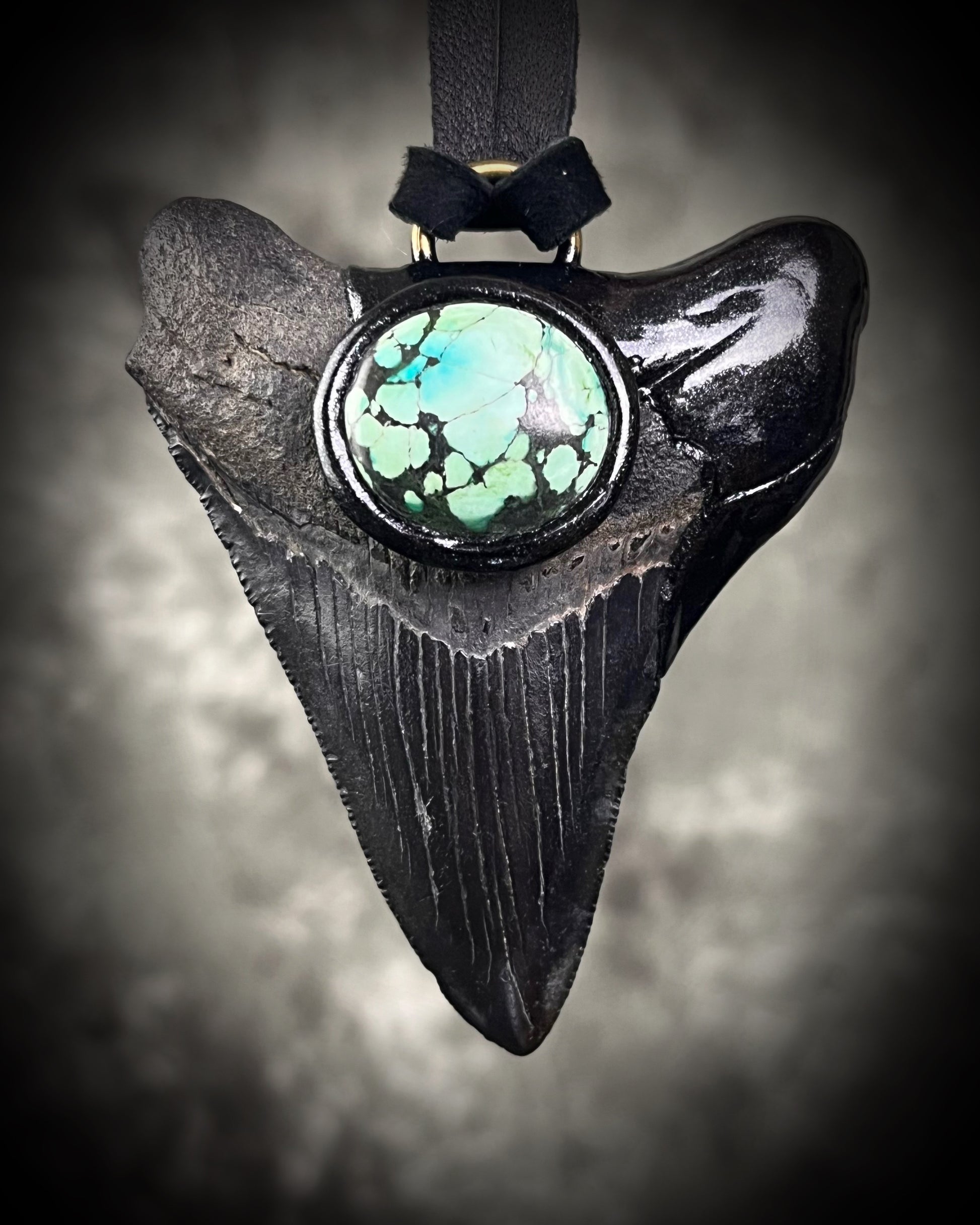 Handmade megalodon tooth talisman with natural turquoise accents, black finish, and black leather cord, featuring a fossilized prehistoric shark tooth transformed into a bold statement necklace.