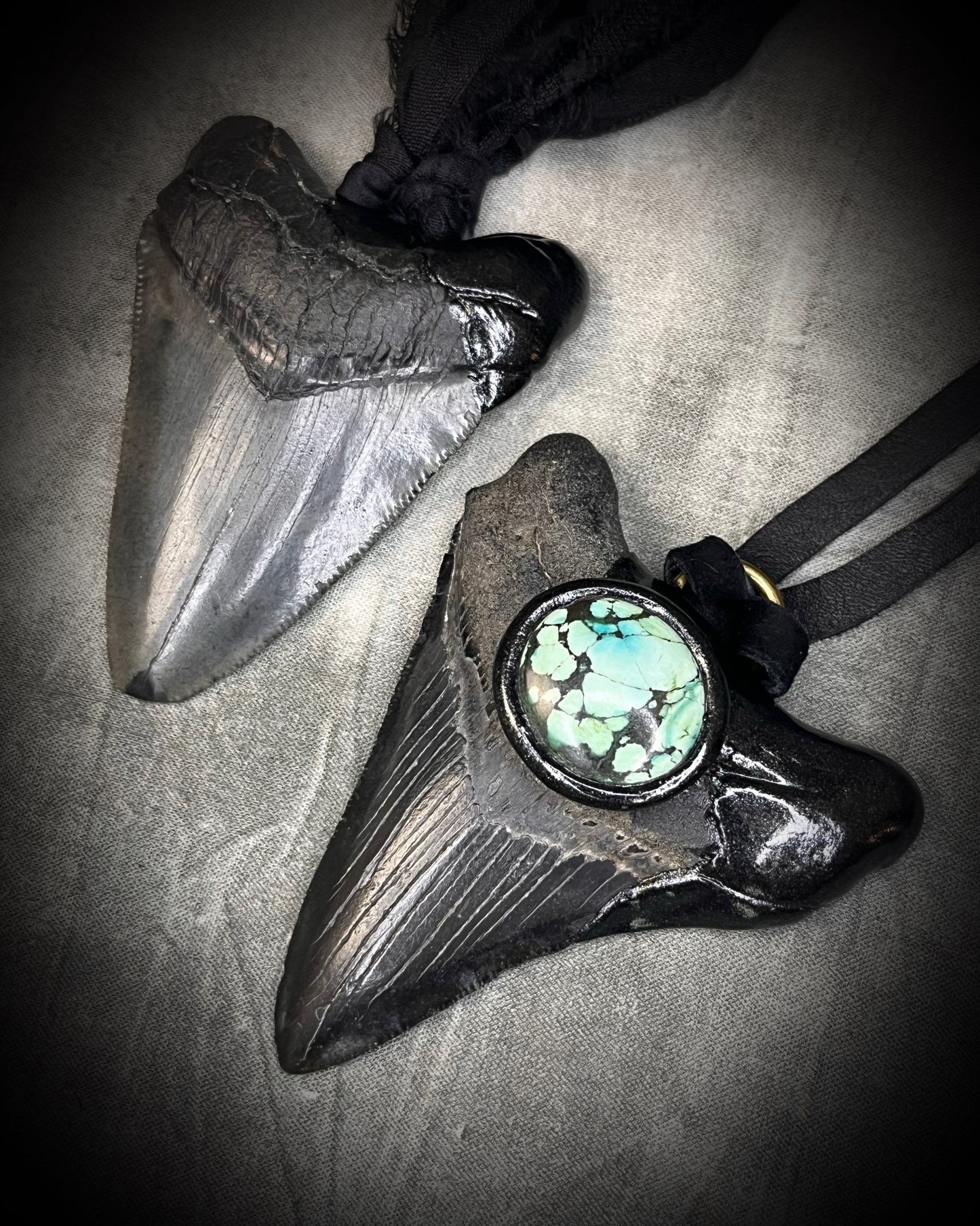 Handmade megalodon tooth talisman with natural turquoise accents, black finish, and black leather cord, featuring a fossilized prehistoric shark tooth transformed into a bold statement necklace.