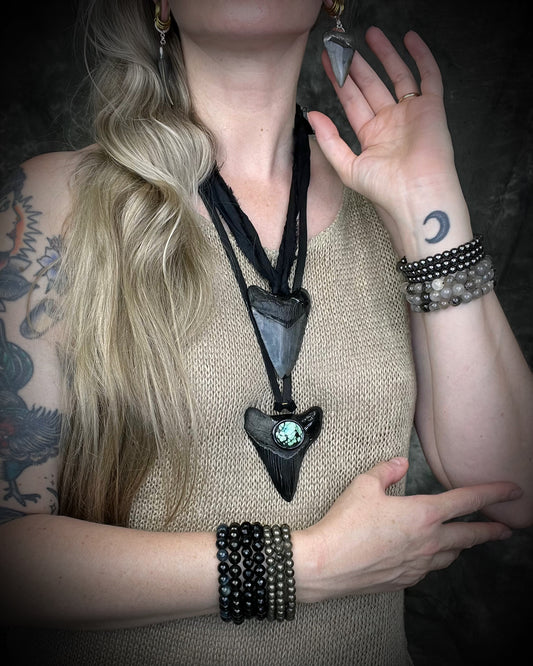 Handmade megalodon tooth talisman with natural turquoise accents, black finish, and black leather cord, featuring a fossilized prehistoric shark tooth transformed into a bold statement necklace.