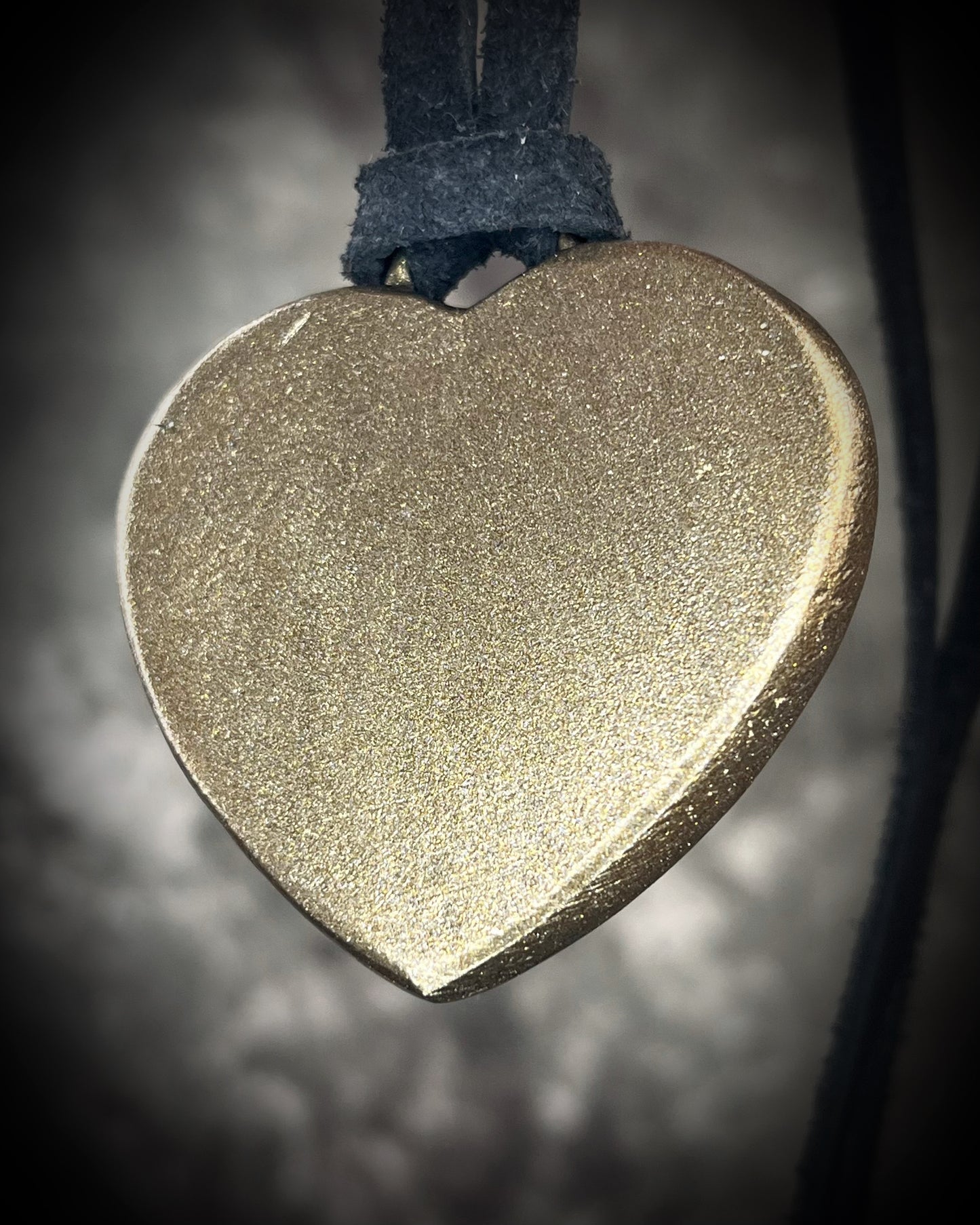 Heart-shaped gold pendant on a dark background. backside of handmade crystal healing mahogany obsidian heart pendant gift for her. 