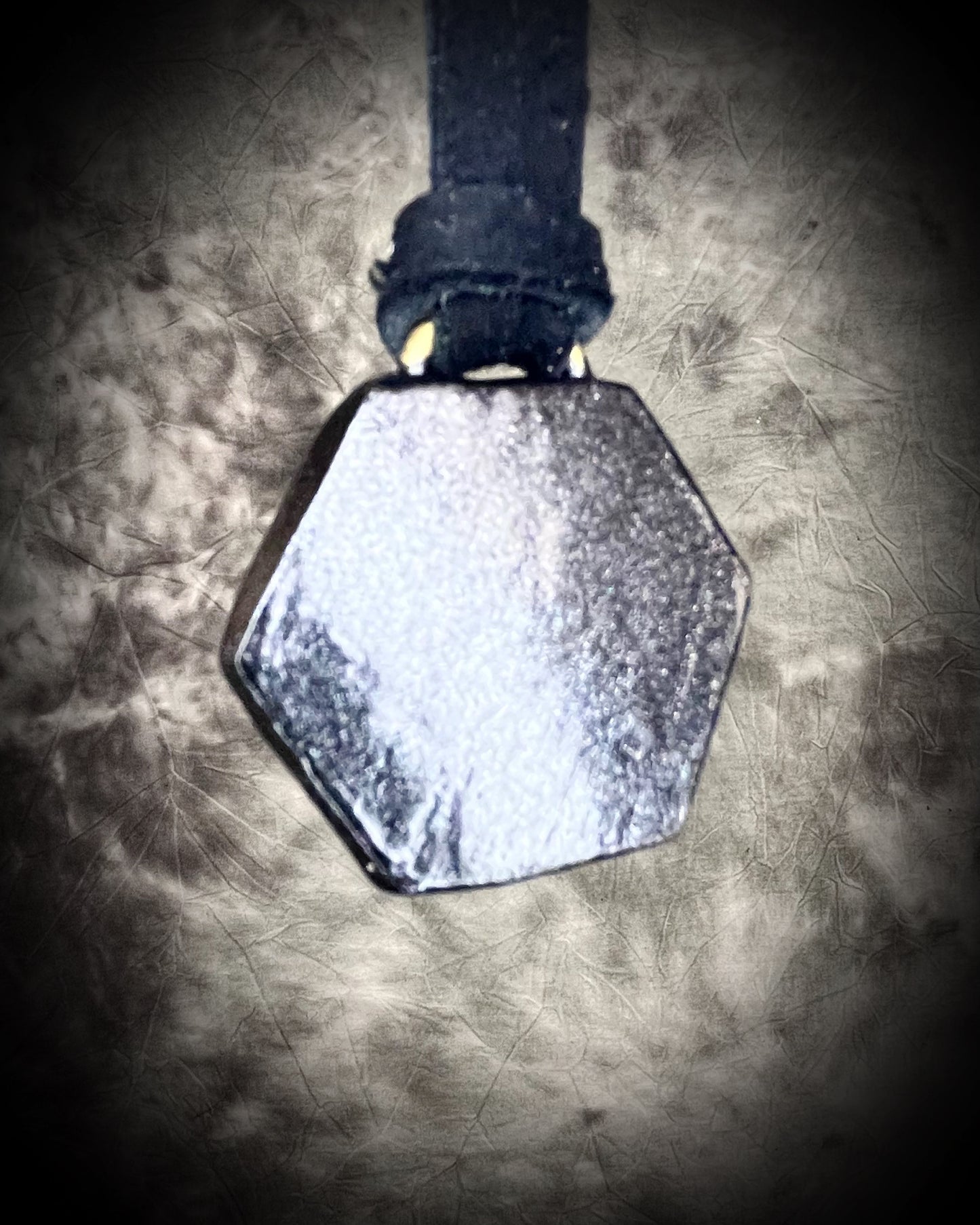 Hexagonal black witchy metallic necklace on black leather on a textured surface