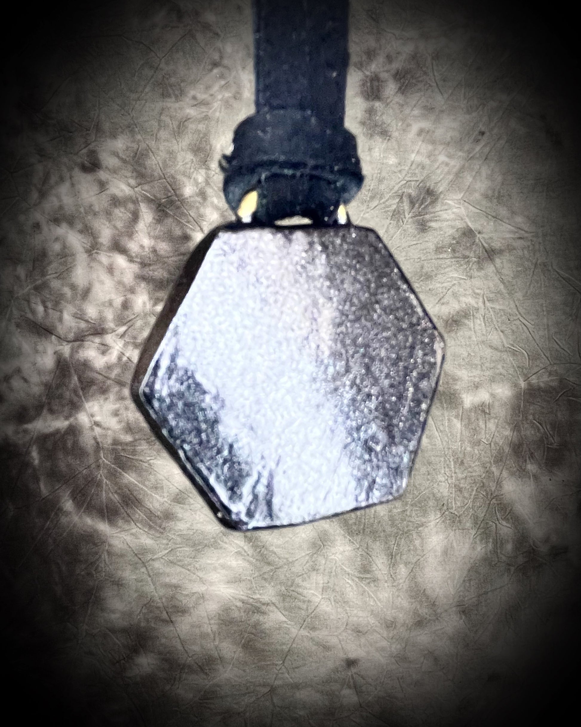 Hexagonal black witchy metallic necklace on black leather on a textured surface