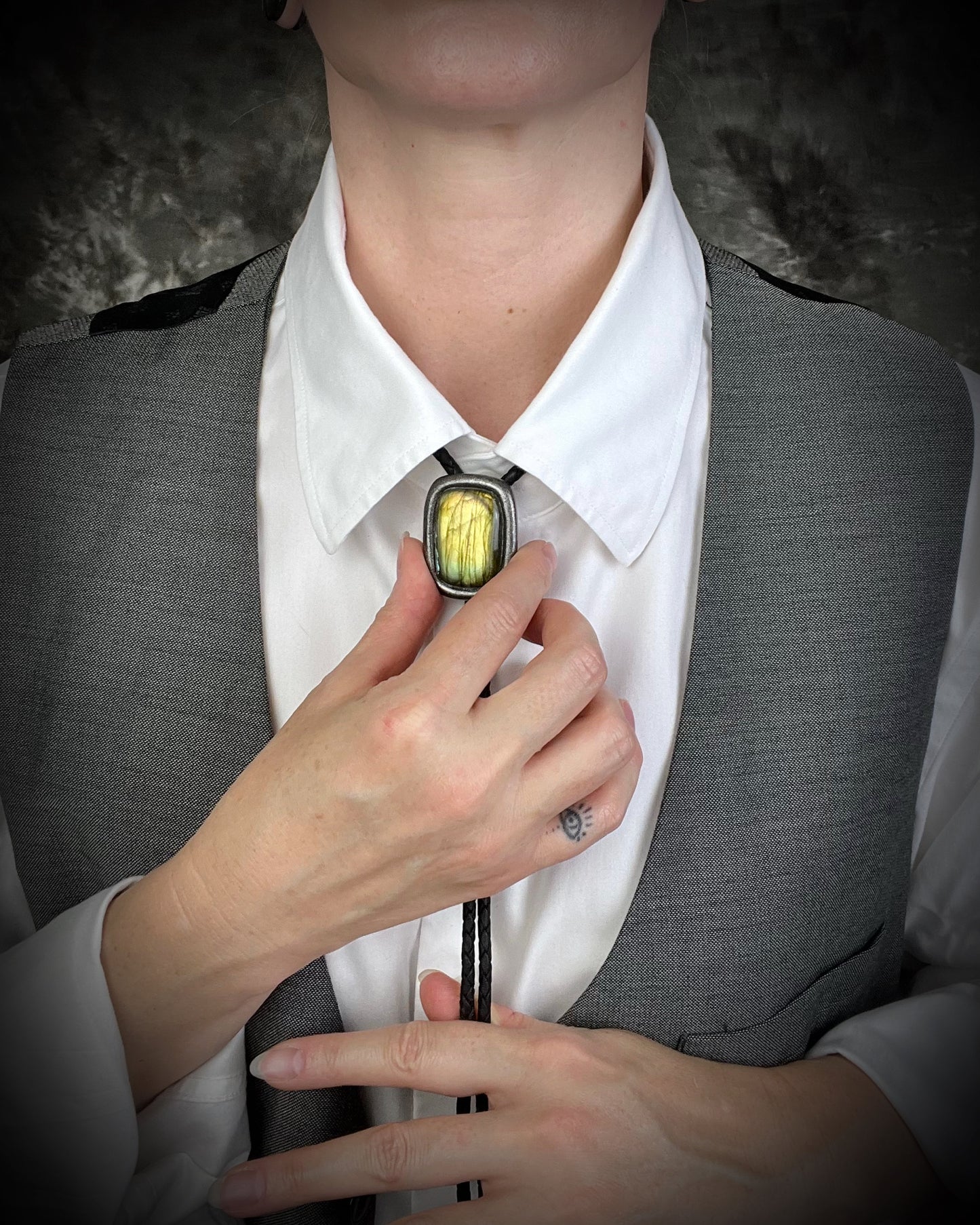 Person adjusting a labradorite crystal bolo tie with a glowing stone on a dark background