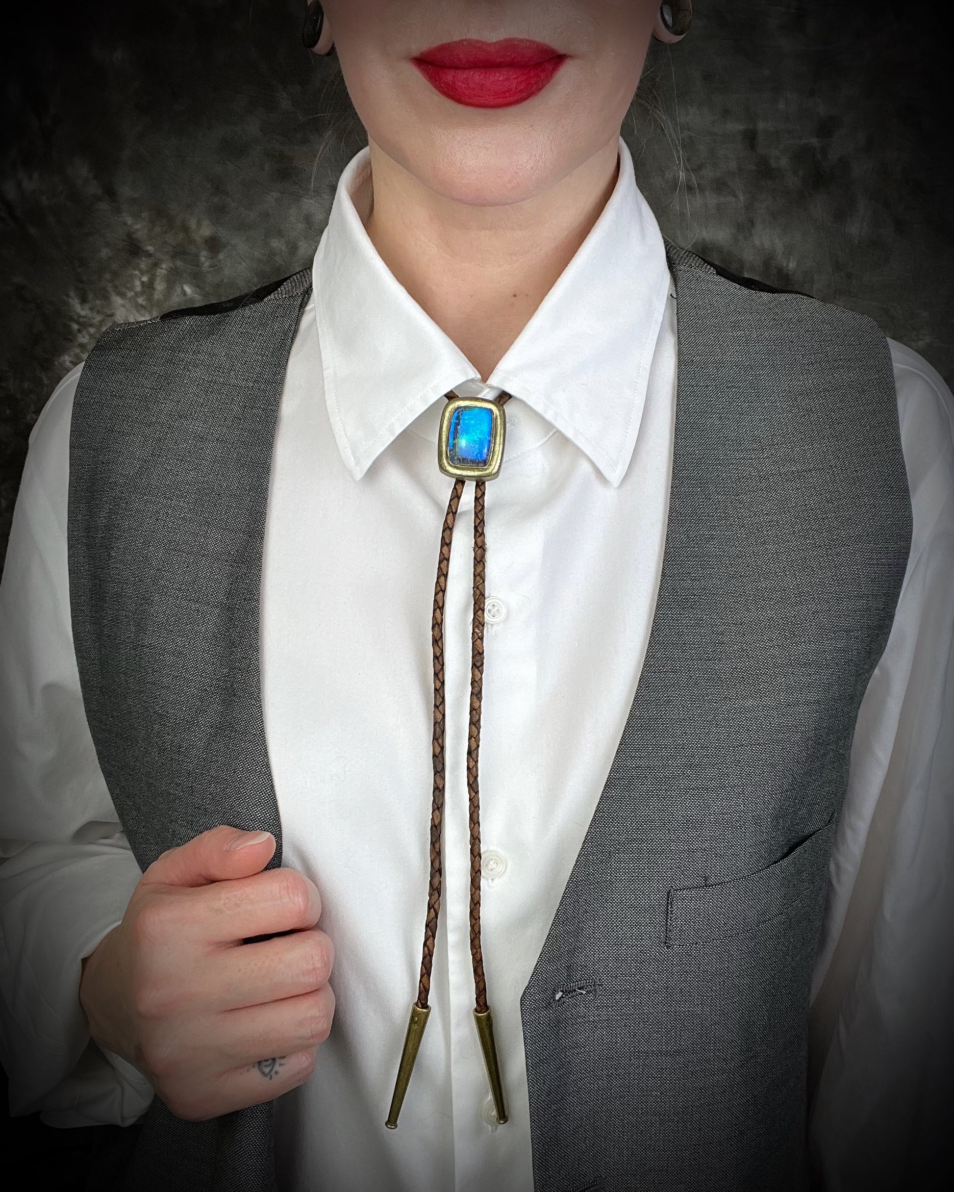 Model wearing a suit with a vest and Labradorite and Quartz doublet gold bolo tie on brown leather – artisan crystal bolo necklace, mystical men’s bolo tie, handmade gemstone statement jewelry.