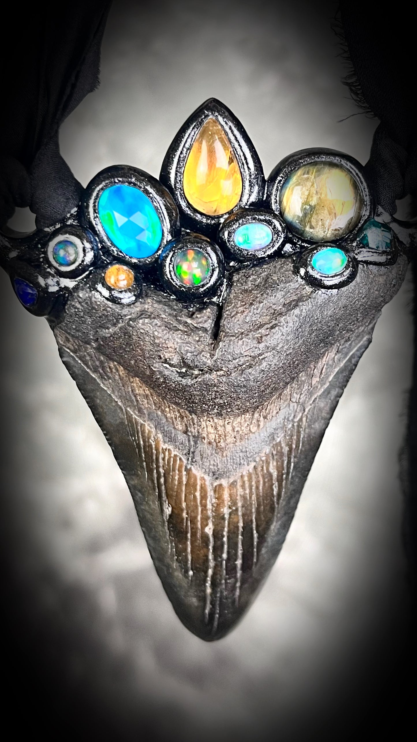 Large megalodon tooth necklace crowned with citrine, opal, black opal, labradorite, dioptase, golden tourmaline, lapis lazuli, and moonstone — set in black and hung from recycled silk ribbons.
