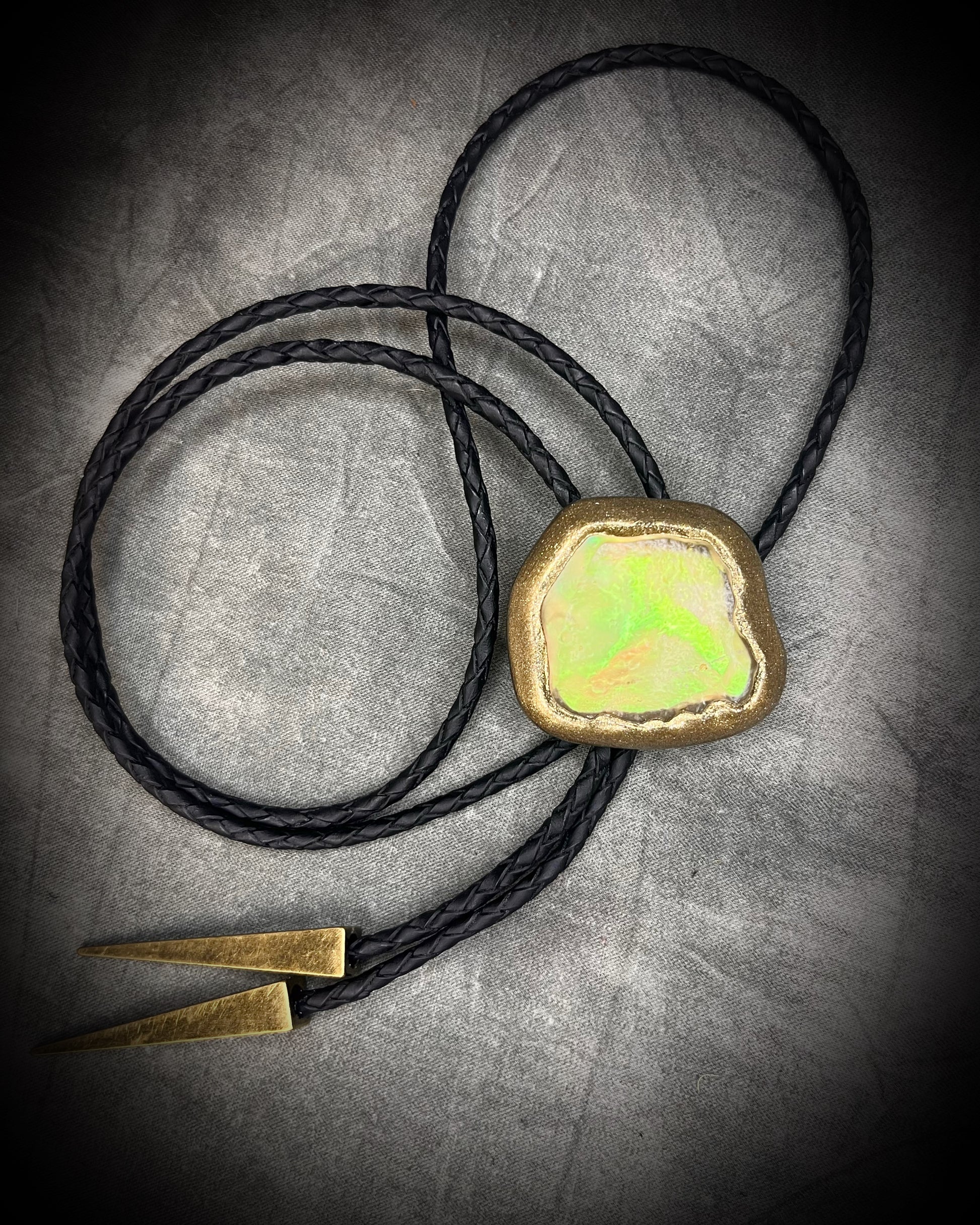 Libyan Desert Glass bolo tie with sculpted gold finish, black leather cord, and gold spike bolo tips by Become Spellbound, Baltimore Magazine Best of Baltimore 2026 Jewelry winner.