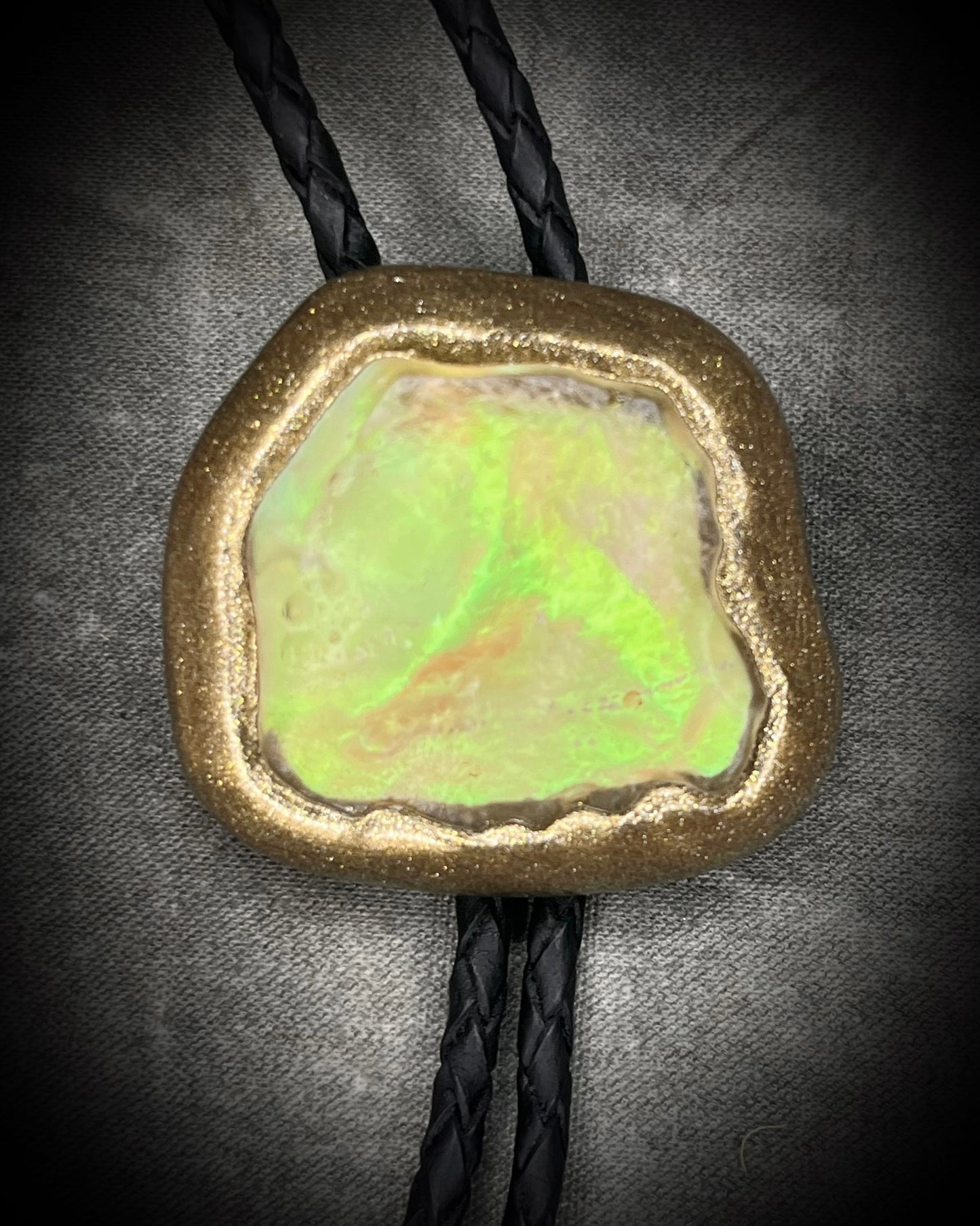 Libyan Desert Glass bolo tie with sculpted gold finish, black leather cord, and gold spike bolo tips by Become Spellbound, Baltimore Magazine Best of Baltimore 2026 Jewelry winner.