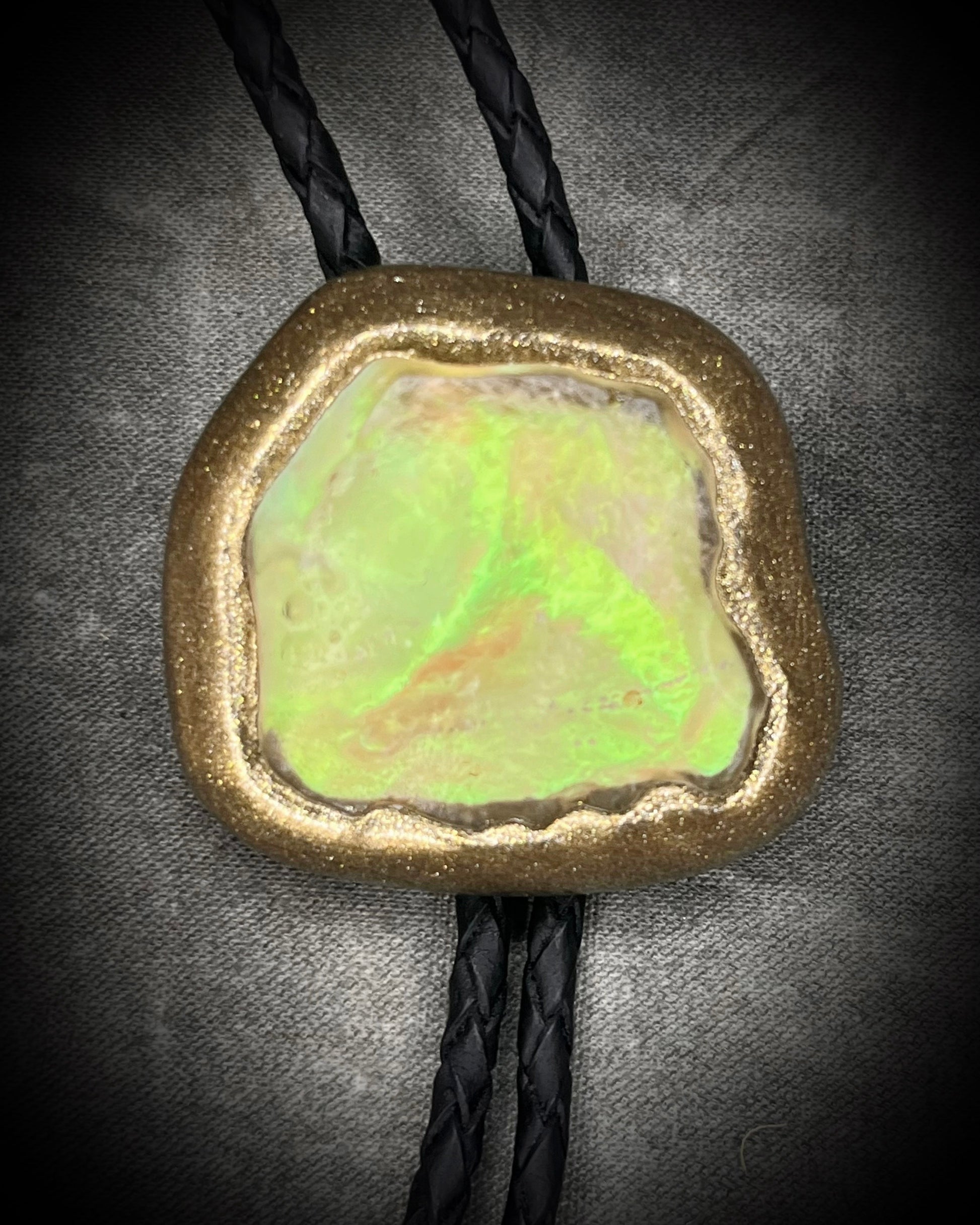 Libyan Desert Glass bolo tie with sculpted gold finish, black leather cord, and gold spike bolo tips by Become Spellbound, Baltimore Magazine Best of Baltimore 2026 Jewelry winner.