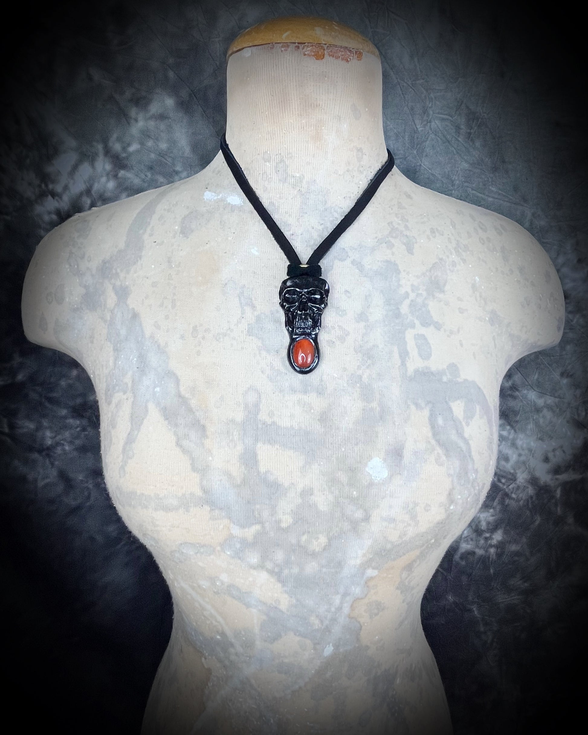 Mannequin wearing black skull and orange carnelian crystal talisman on black leather cord, gothic and mystical jewelry for fall, cosplay, renaissance festival, handcrafted statement necklace.