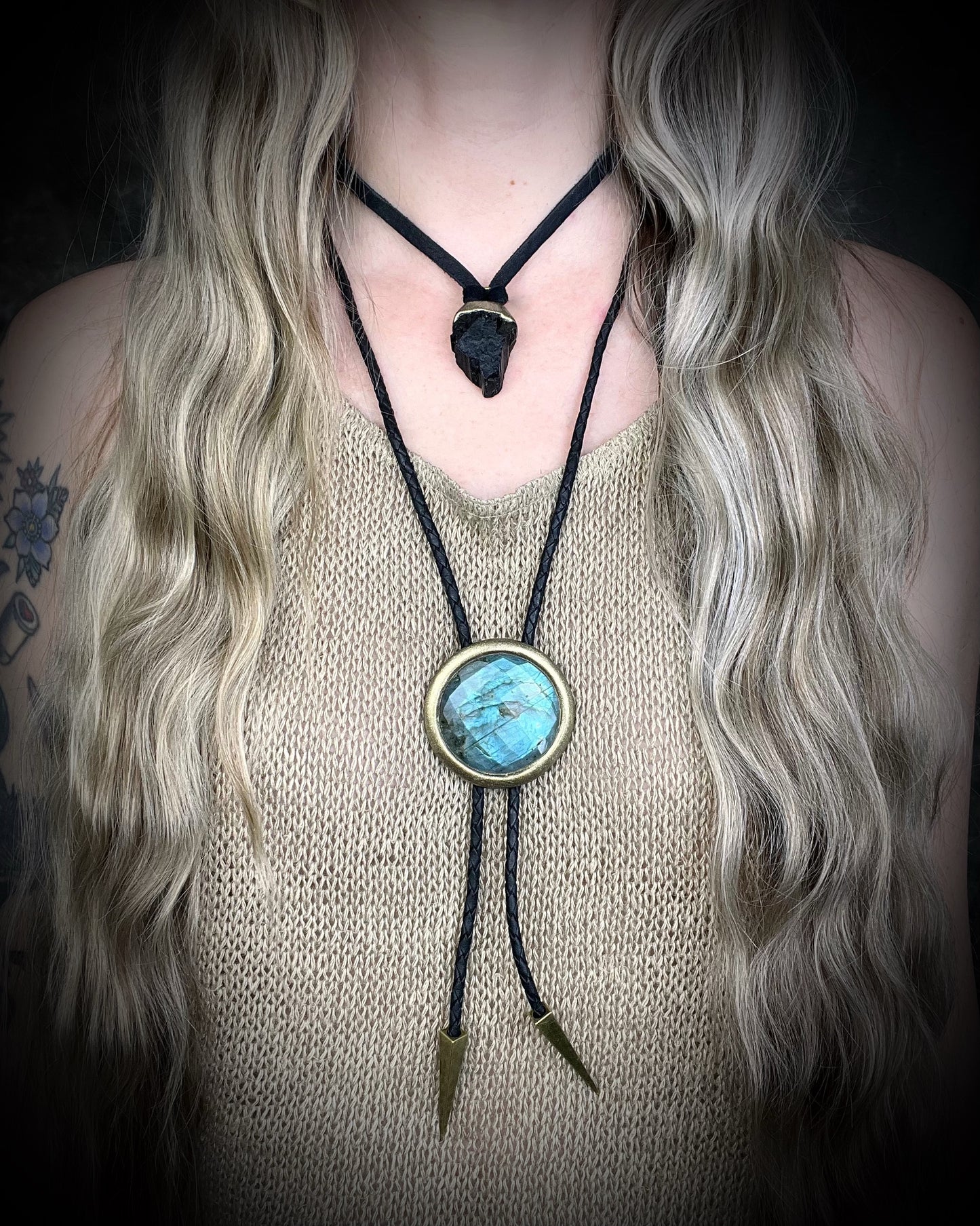 Person wearing a bolo tie with a blue stone and black cord, against a dark background.