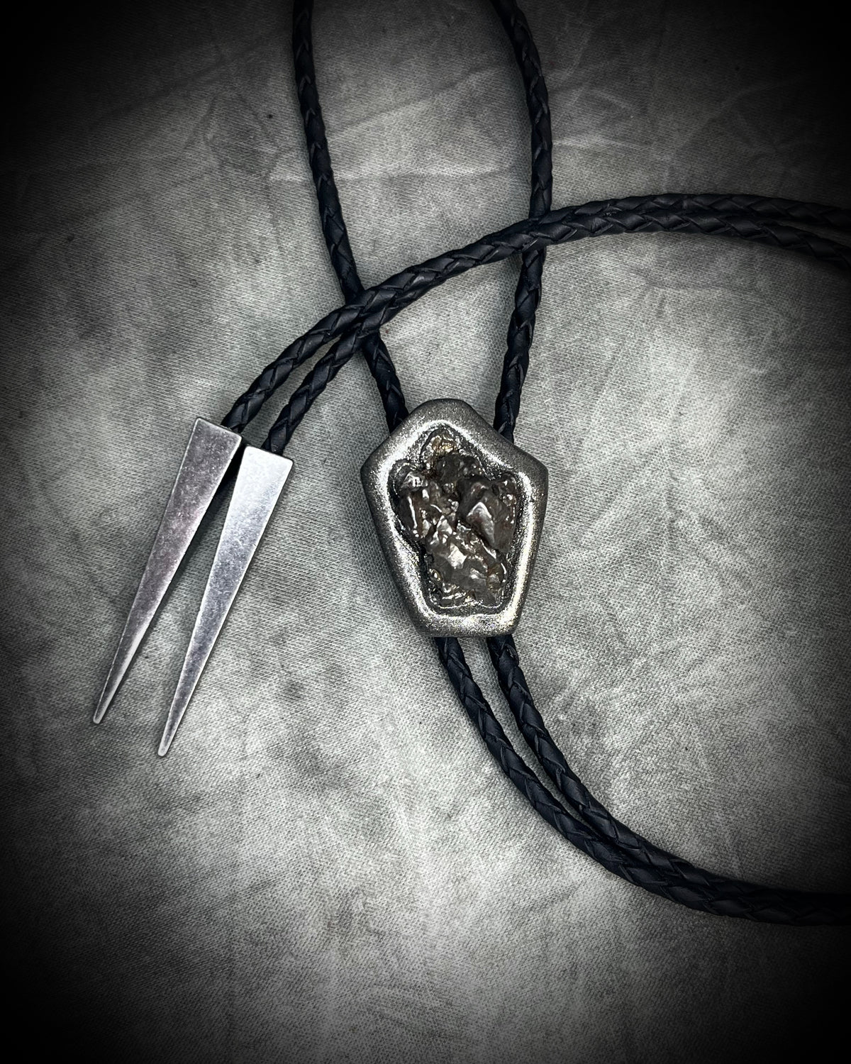 Meteorite bolo tie with gunmetal finish, black leather cord, and dramatic spike bolo tips, handmade by Become Spellbound in Baltimore, Maryland.