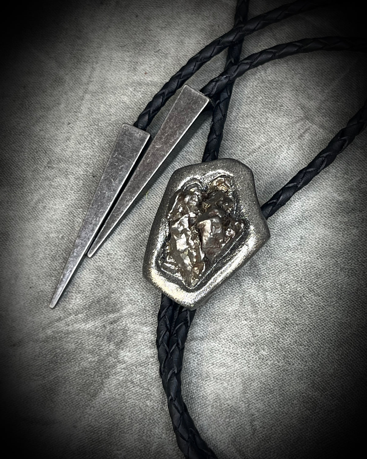 Meteorite bolo tie with gunmetal finish, black leather cord, and dramatic spike bolo tips, handmade by Become Spellbound in Baltimore, Maryland.