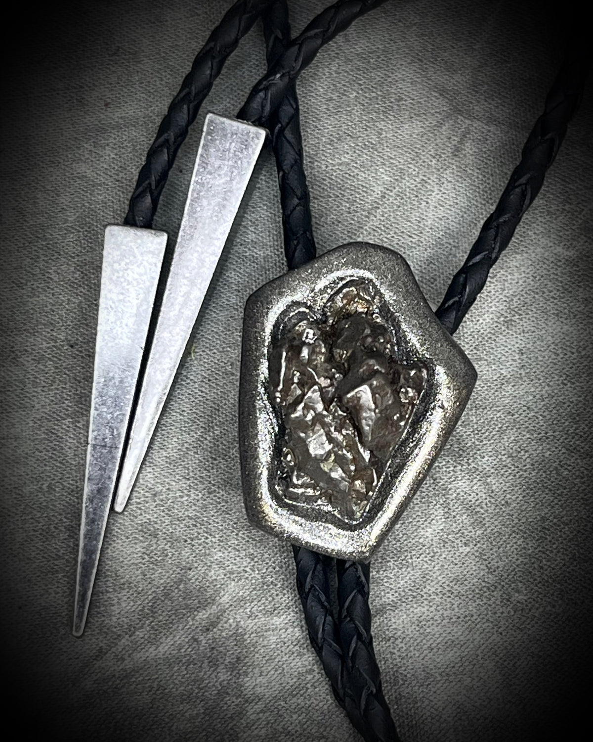 Meteorite bolo tie with gunmetal finish, black leather cord, and dramatic spike bolo tips, handmade by Become Spellbound in Baltimore, Maryland.