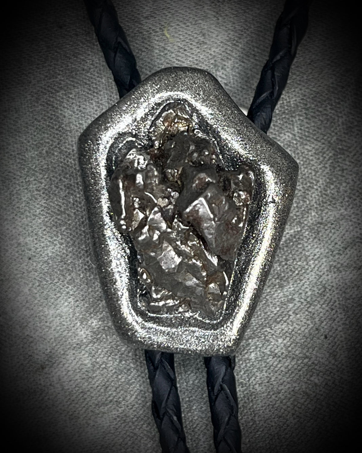 Meteorite bolo tie with gunmetal finish, black leather cord, and dramatic spike bolo tips, handmade by Become Spellbound in Baltimore, Maryland.